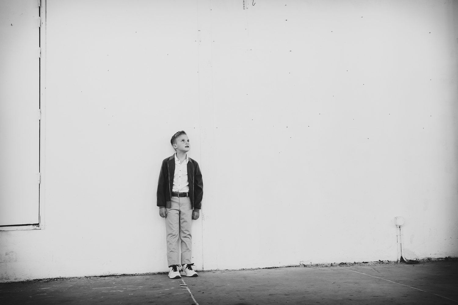Een jonge jongen staat voor een witte muur en kijkt omhoog.