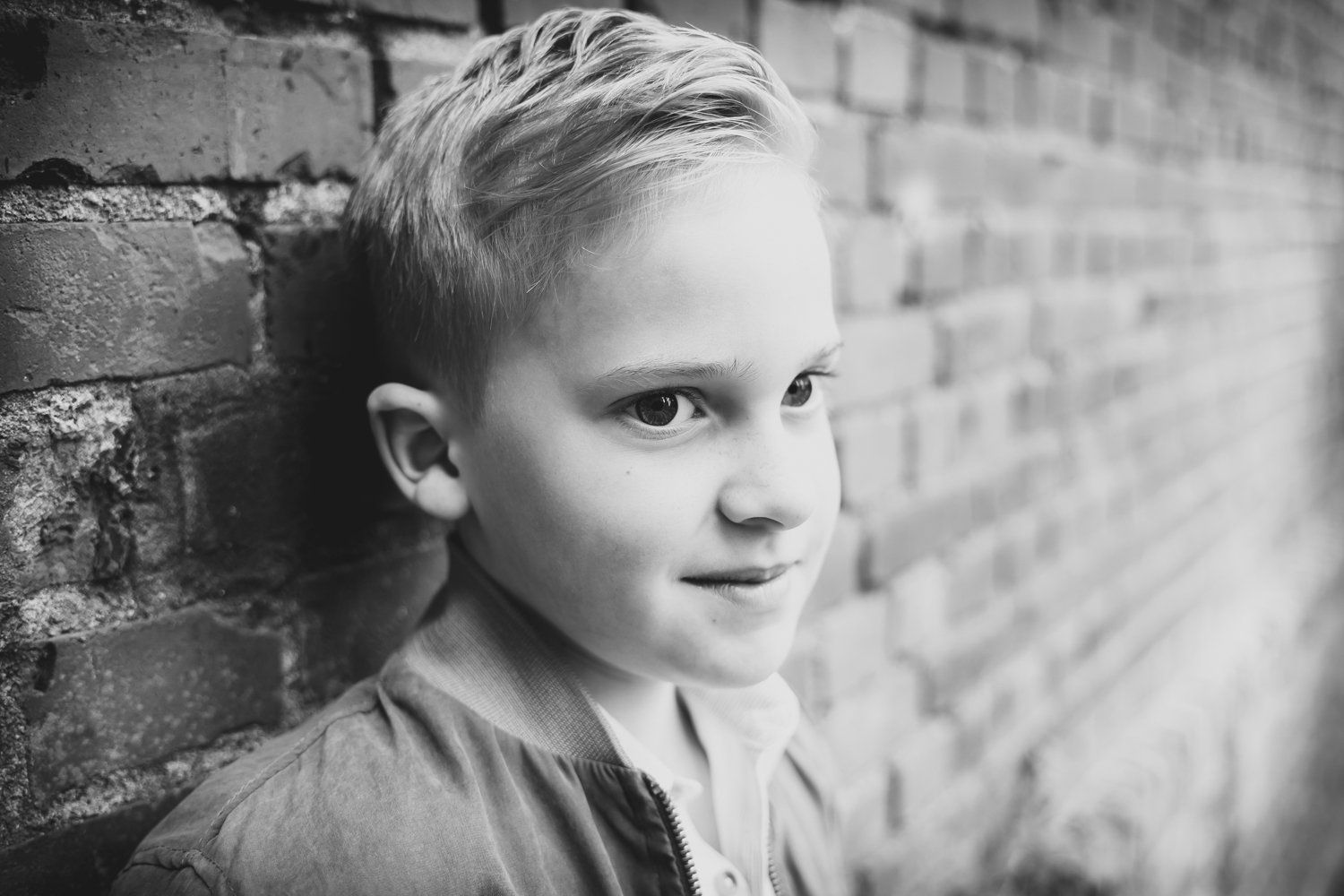 Een jonge jongen leunt tegen een bakstenen muur op een zwart-witfoto.