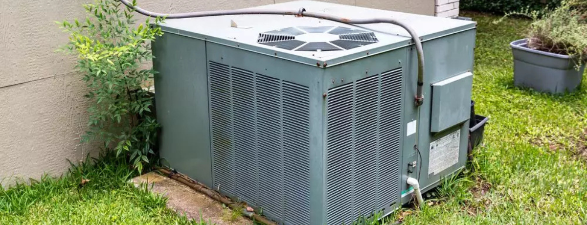 An air conditioner is sitting in the grass next to a wall.