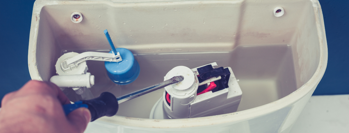A person is fixing a toilet with a screwdriver.