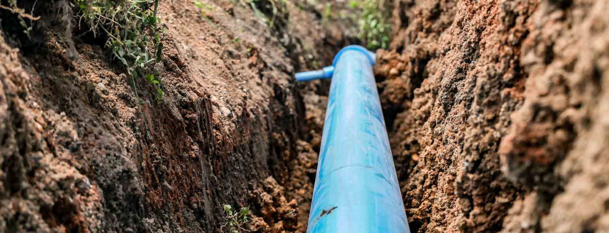 A blue pipe is laying in the dirt in a trench.