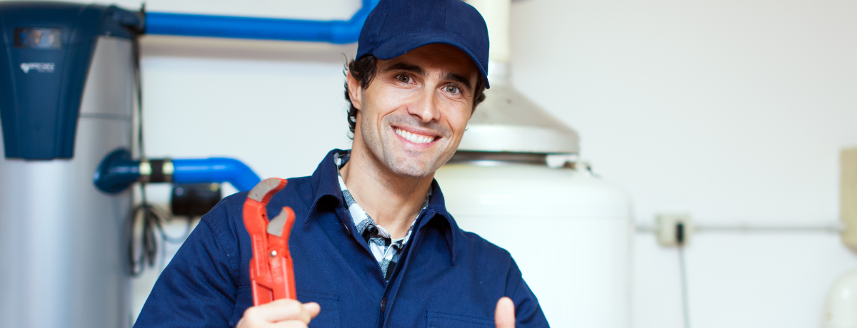 A smiling plumber is holding a wrench and giving a thumbs up.