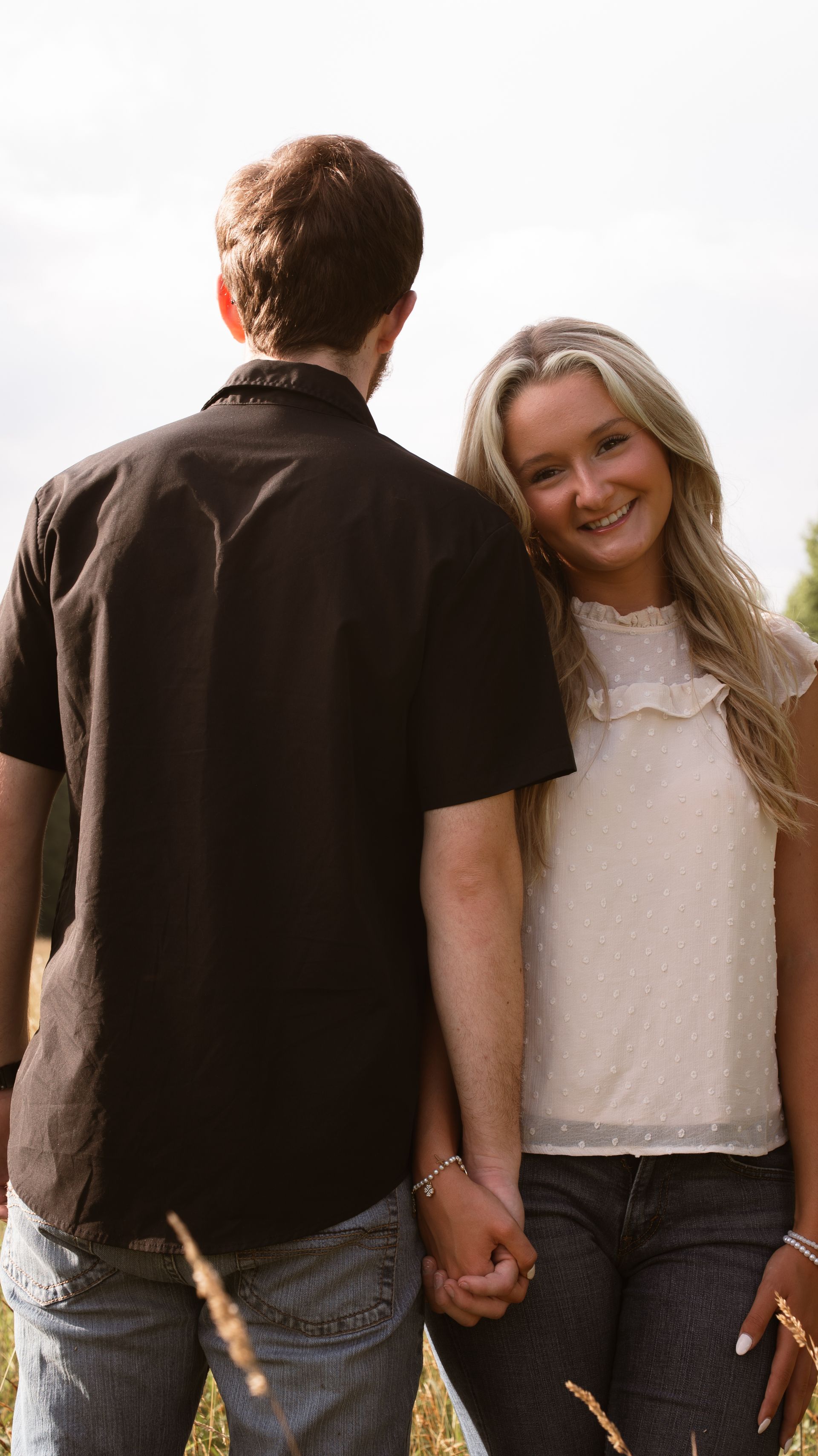 A woman faces the camera smiling, holding her boyfriend's hand, who faces away from the camera.