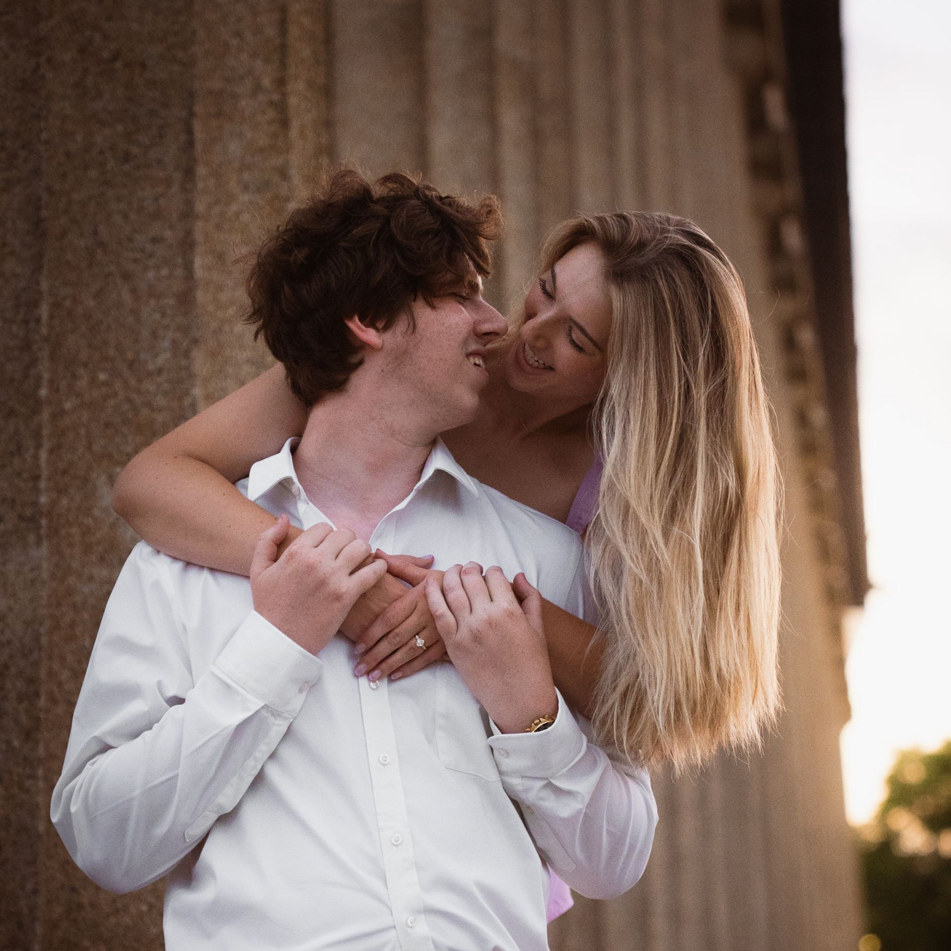A couple hugging and looking into each others' eyes at sunset outside the Parthenon.
