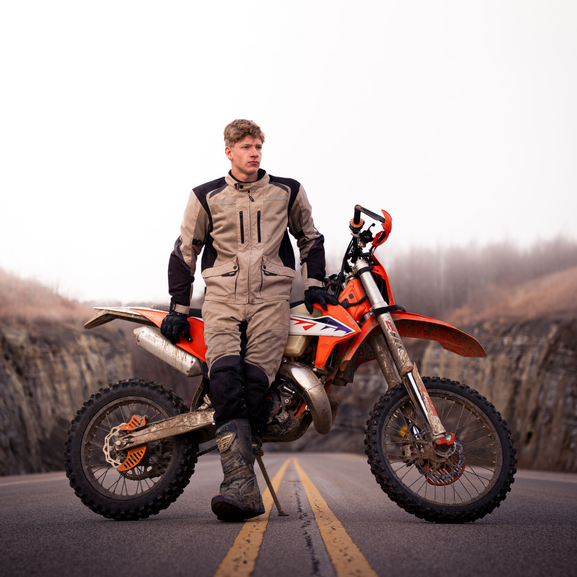 A boy leaning against his dirk bike on a mountain road for senior photos.