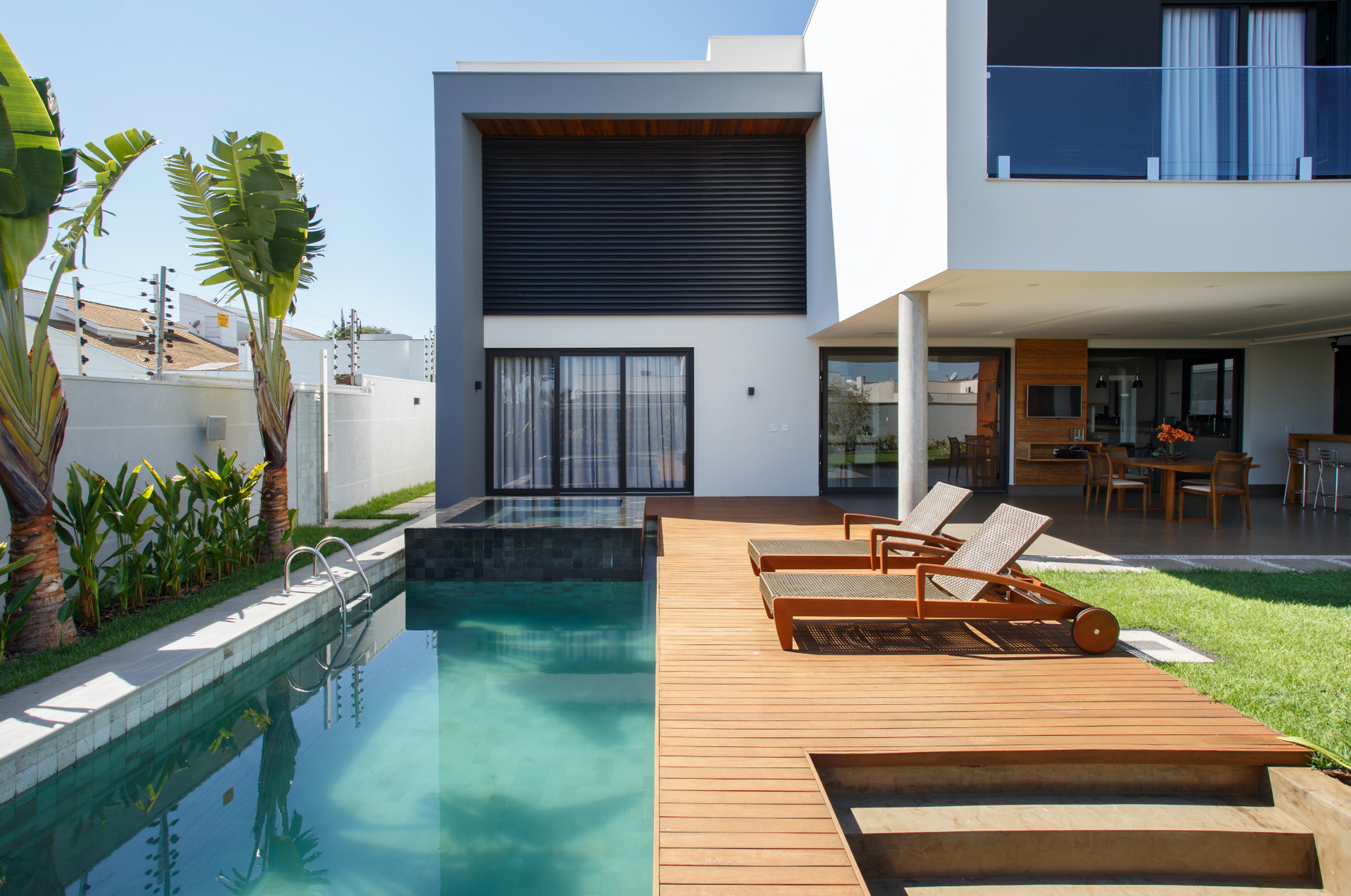 Casa moderna com piscina, deck de madeira e espreguiçadeiras.