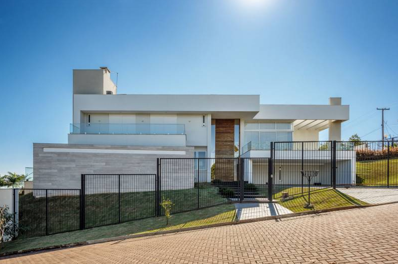 Casa branca moderna com vidro e cerca preta sob céu azul.