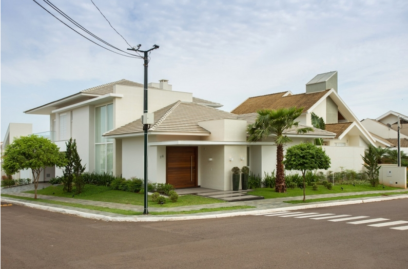 Casa branca moderna em um lote de esquina com uma porta marrom, grama e palmeiras.