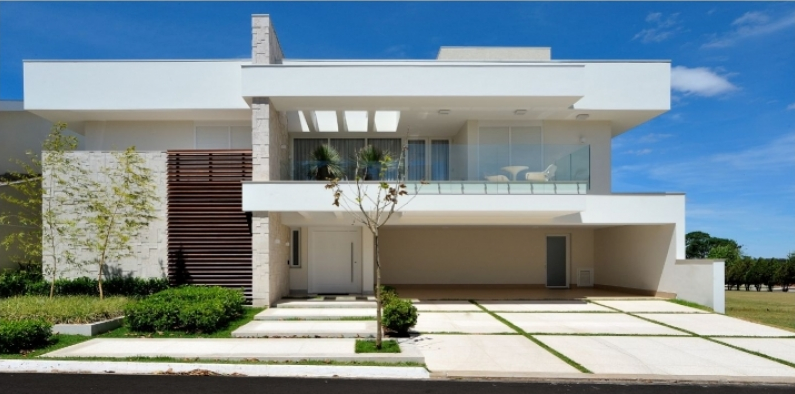 Casa branca moderna com uma porta de madeira, uma garagem e um céu azul.