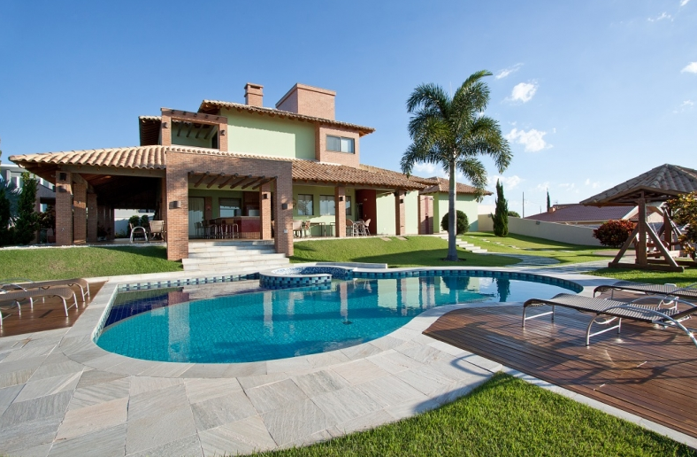 Casa de luxo com piscina e quintal, exterior verde, céu azul, espreguiçadeiras.