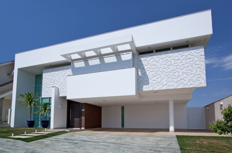 Casa branca moderna com fachada texturizada, garagem coberta e céu azul.