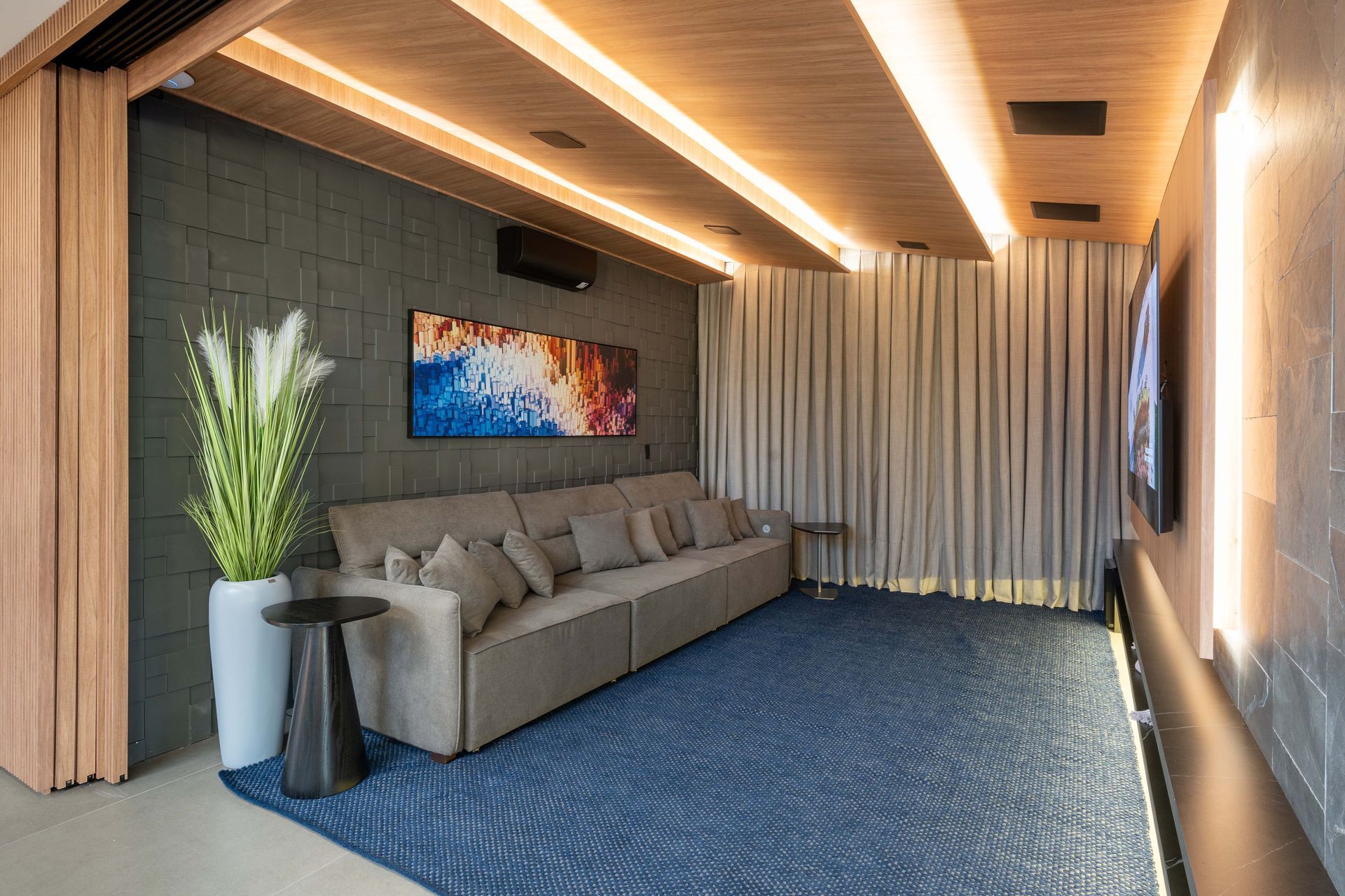 Home theater com sofá cinza, carpete azul, arte e cortinas creme.
