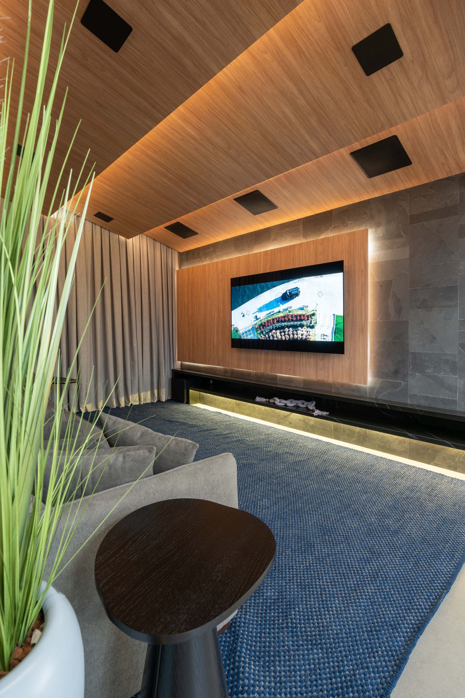 Um home theater moderno com uma TV grande, assentos confortáveis ​​e painéis de madeira no teto.