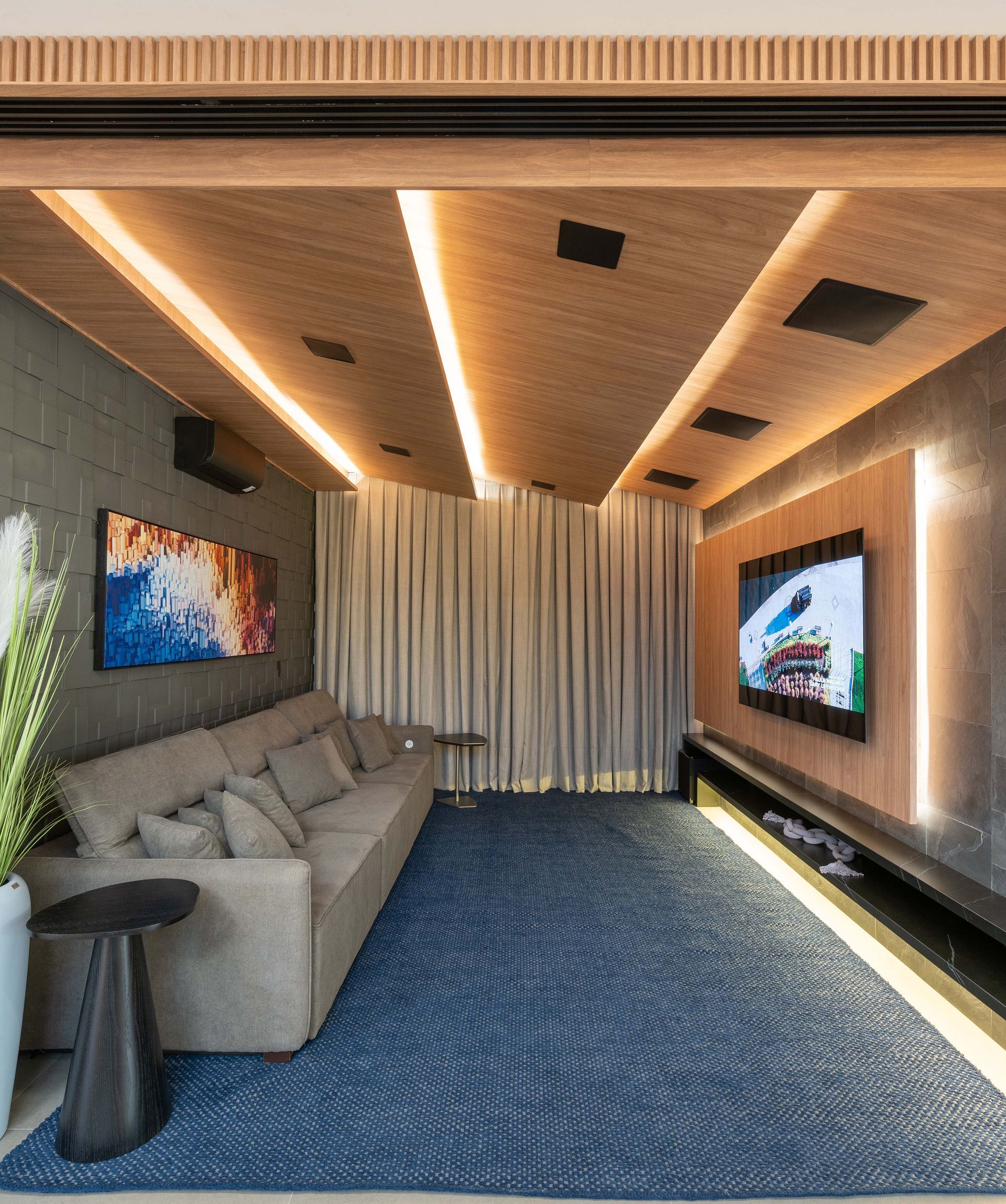 Home theater: carpete azul, sofá cinza, TV grande em uma parede com acabamento em madeira, iluminação embutida.