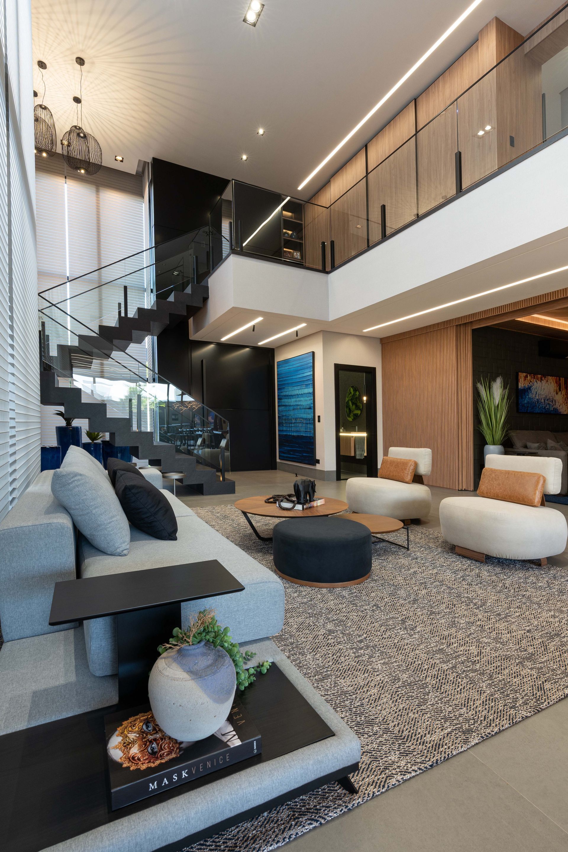 Sala de estar moderna com sofá cinza, tapete estampado e uma escada que leva ao segundo andar.