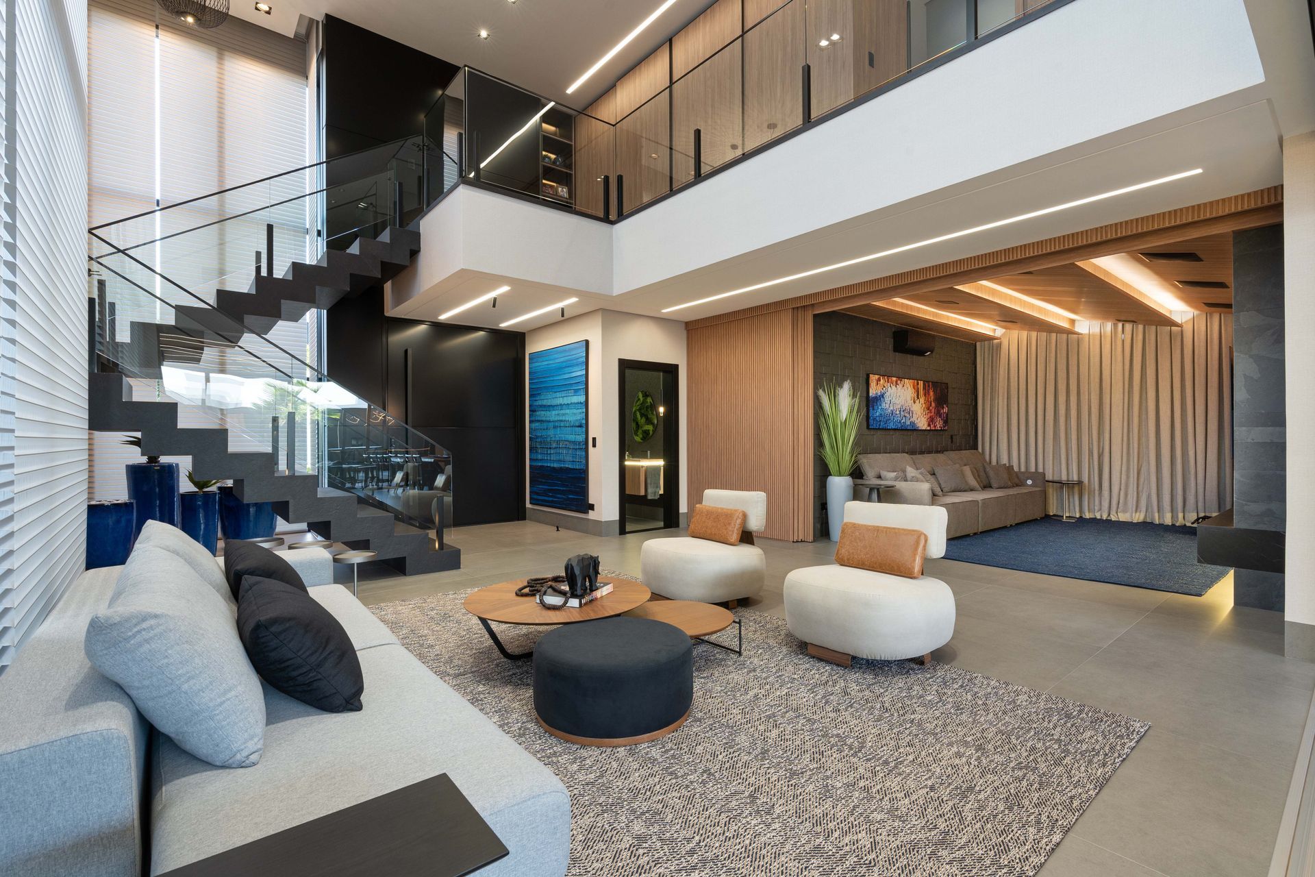 Sala de estar moderna com escada, sofá de cor clara, cadeiras brancas, detalhes em madeira e tapete azul.