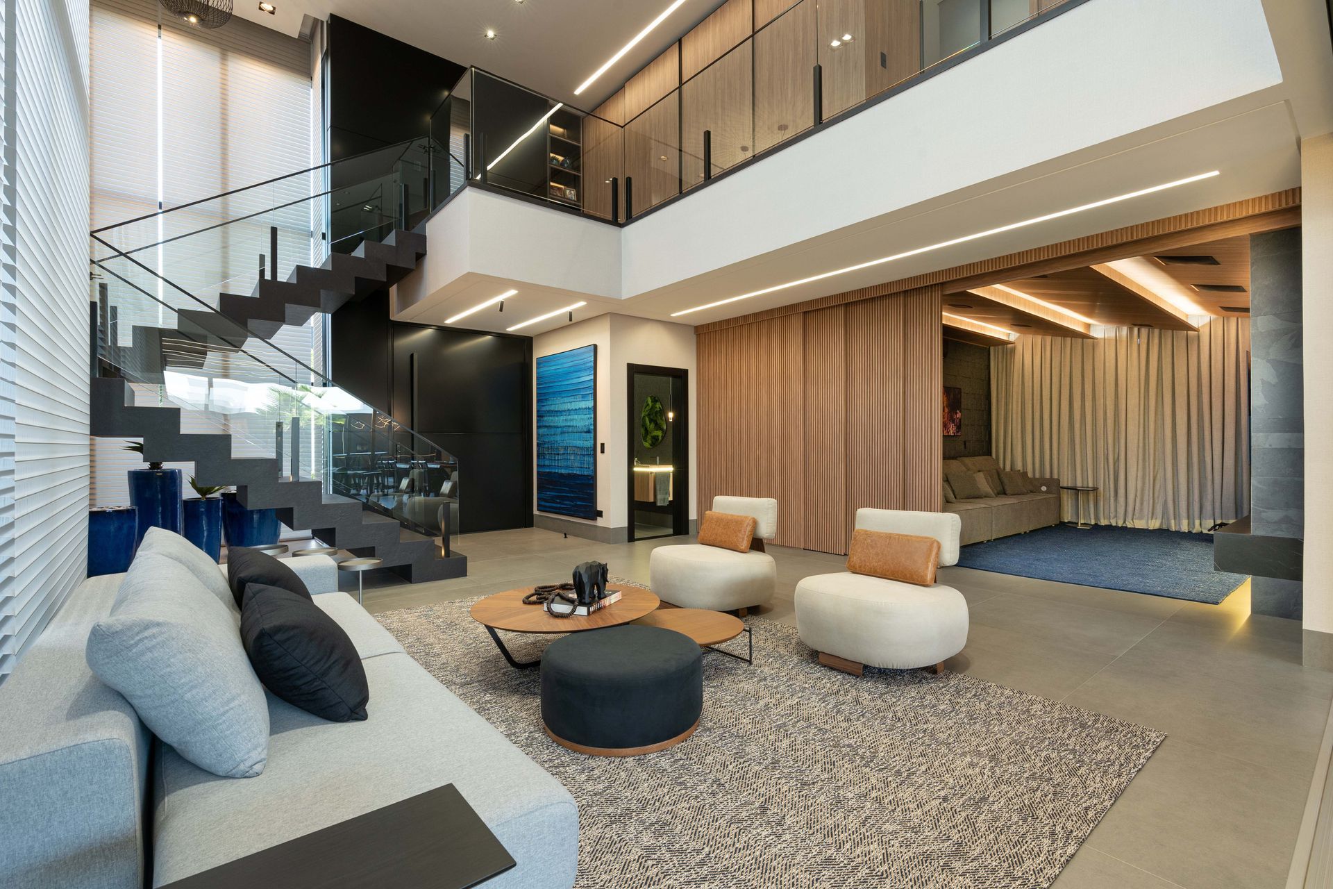 Sala de estar moderna com escada, sofá, poltronas e paleta de cores neutras.