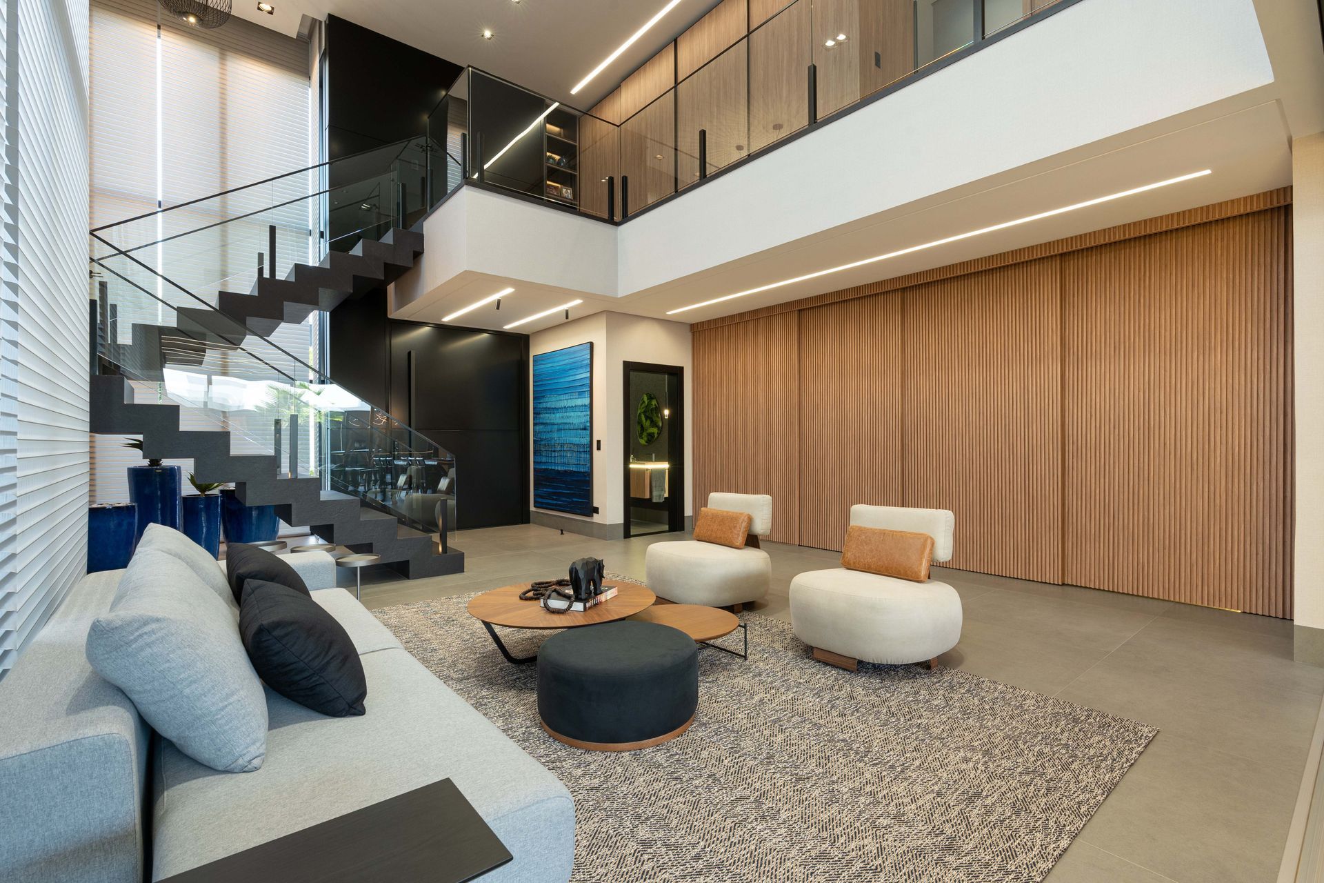 Sala de estar moderna com escada, sofá e poltronas; cores neutras.