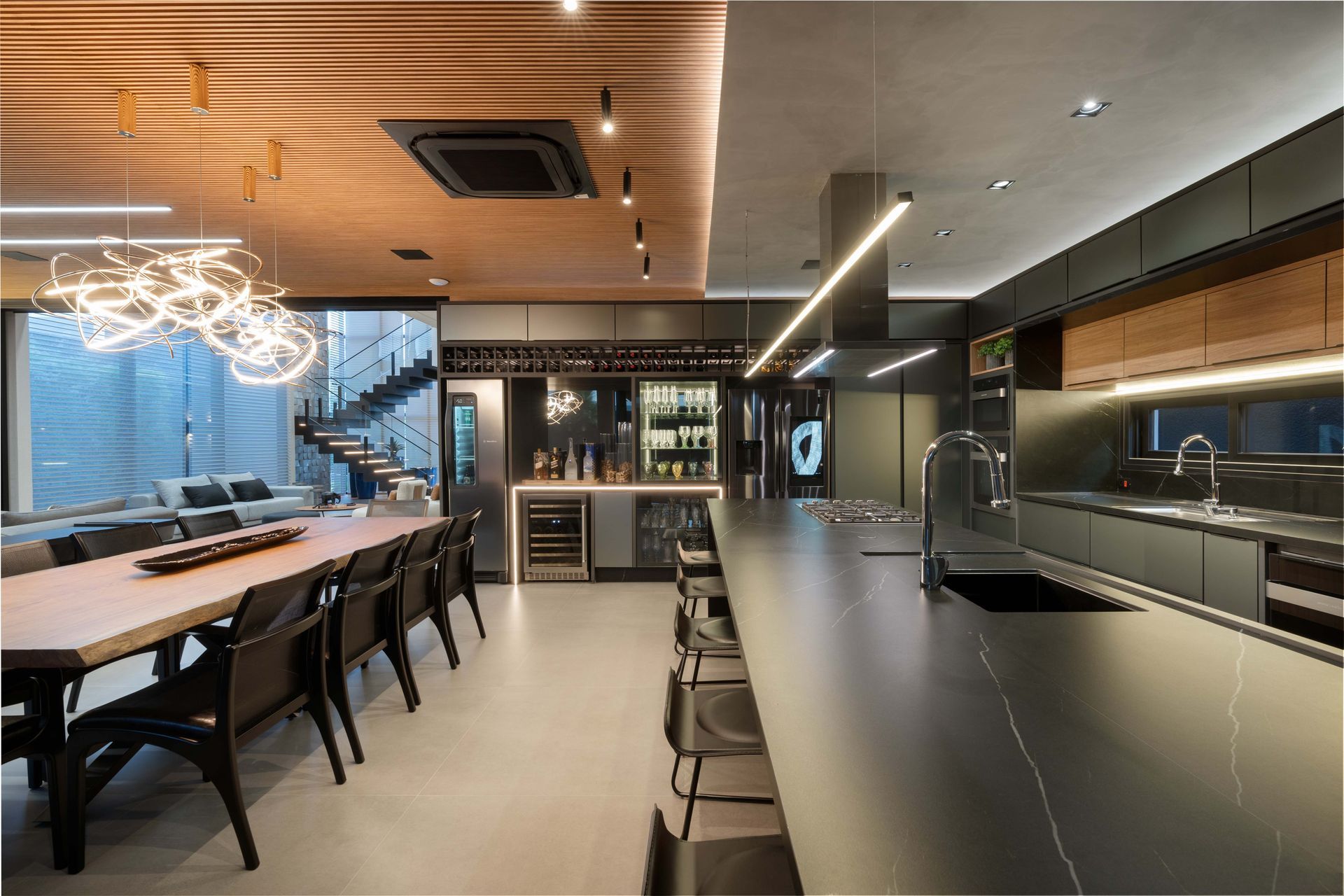 Cozinha e sala de jantar modernas com armários escuros, ilha longa, mesa de jantar e área de bar.