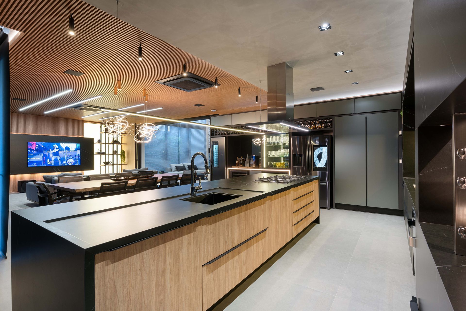 Cozinha moderna com armários de madeira, ilha longa e área de jantar com uma TV grande.