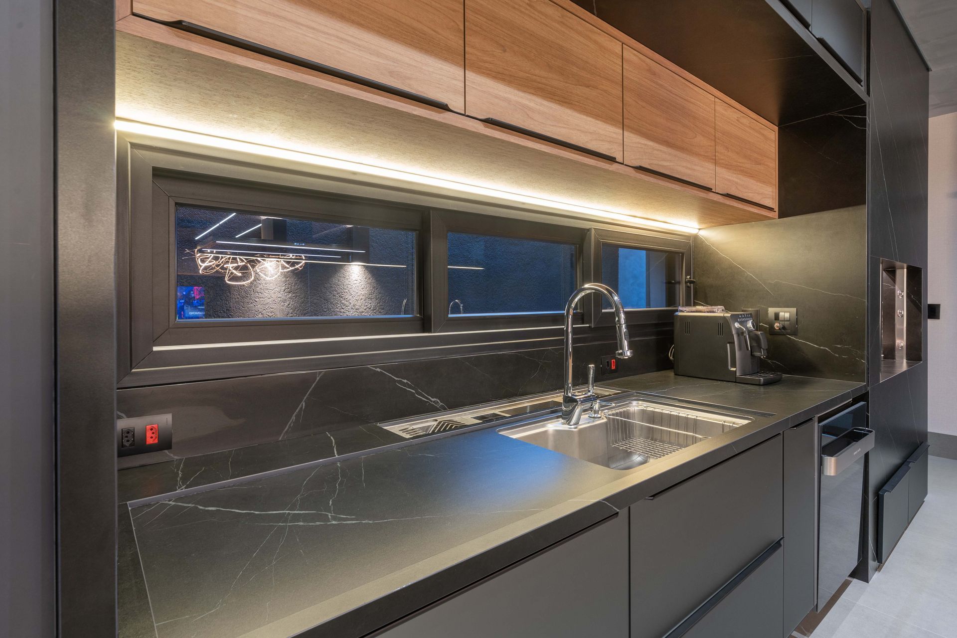 Cozinha moderna com balcões pretos, armários de madeira e iluminação embaixo dos armários.