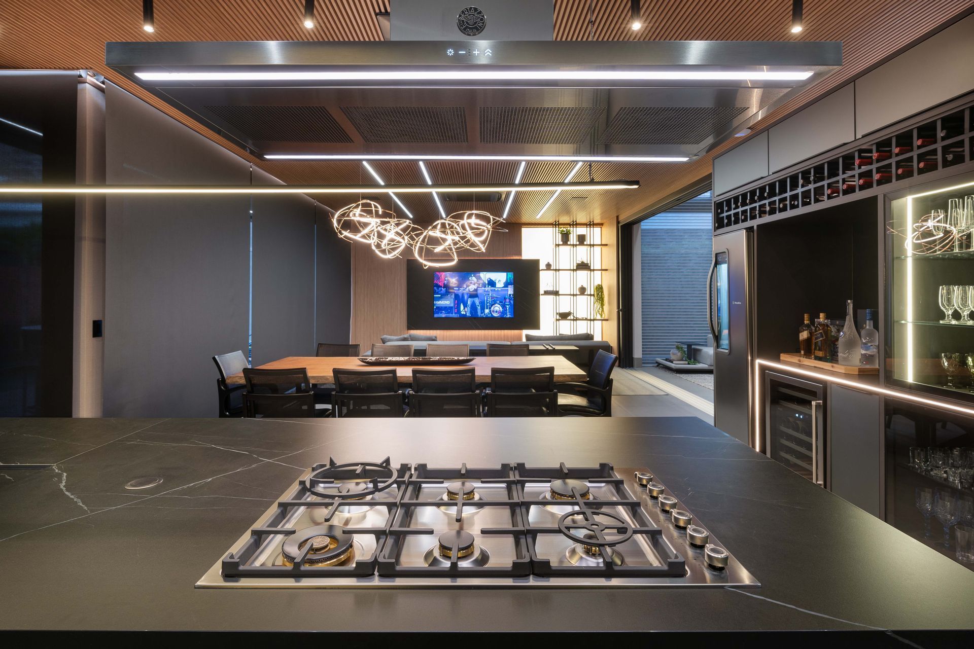 Cozinha moderna com bancadas pretas, fogão a gás, área de jantar e bar com suporte para vinhos.