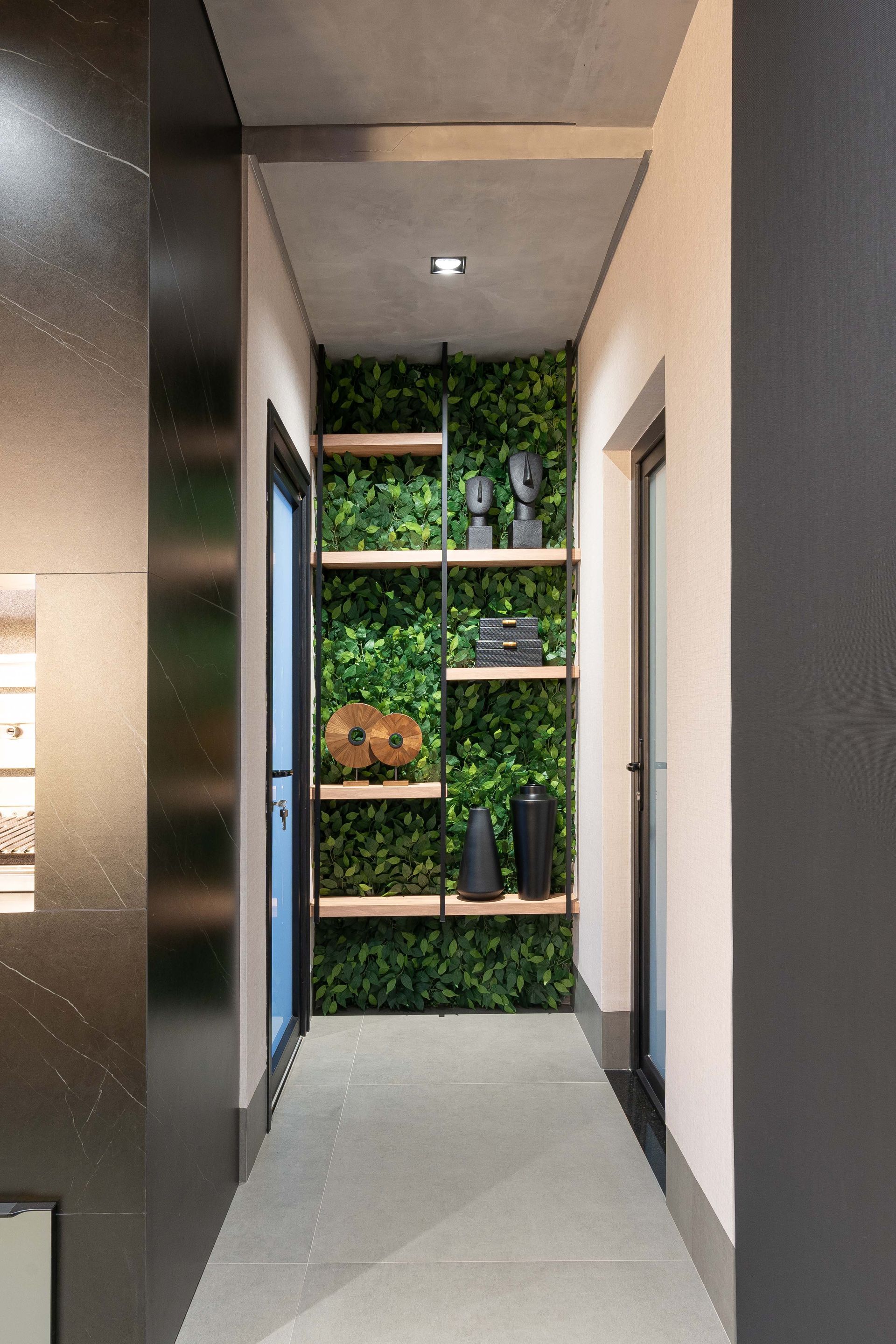 Corredor com parede verde e prateleiras de madeira com decoração. Portas de cada lado.