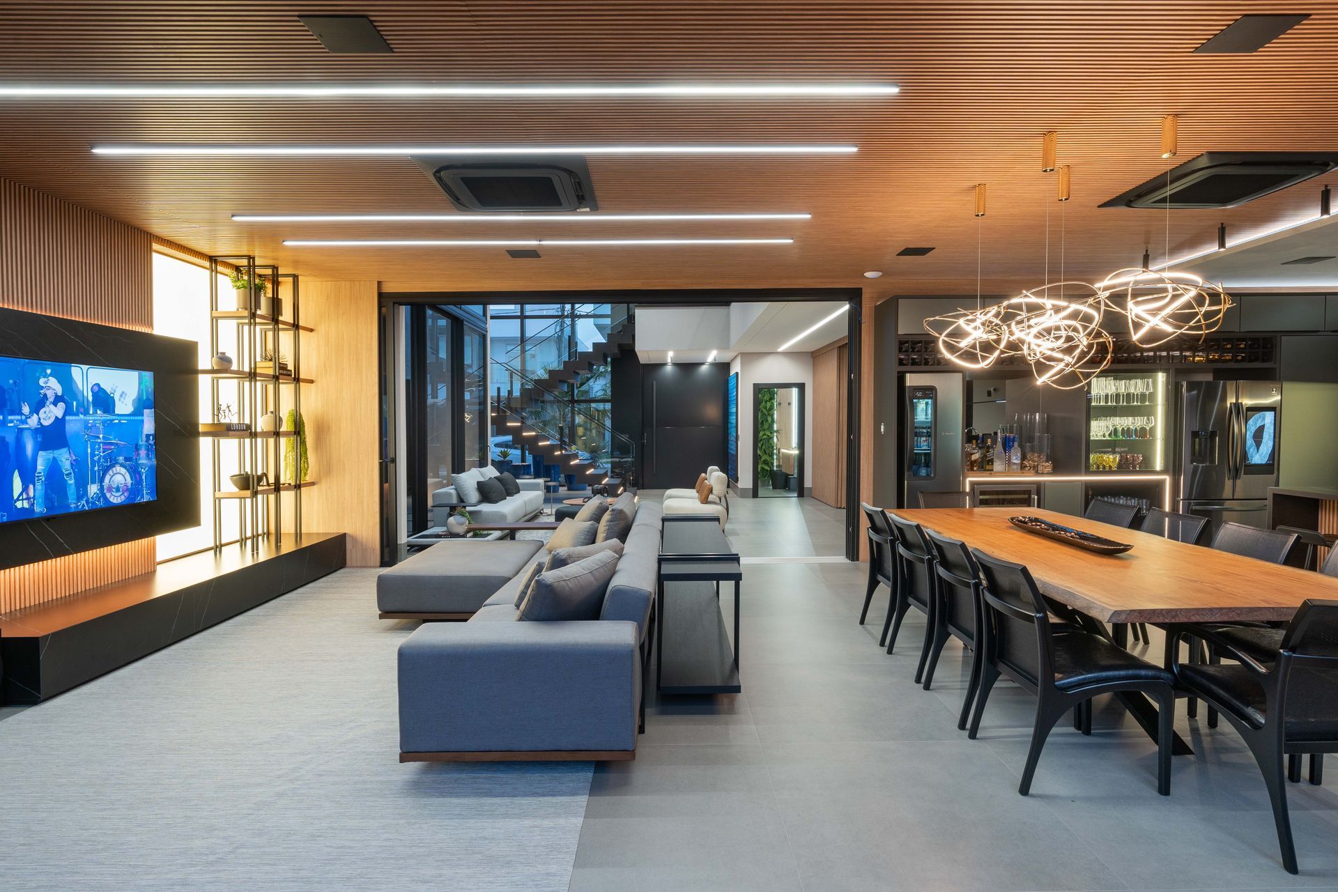 Sala de estar espaçosa com sofás cinza, mesa de jantar de madeira e vista para as escadas.