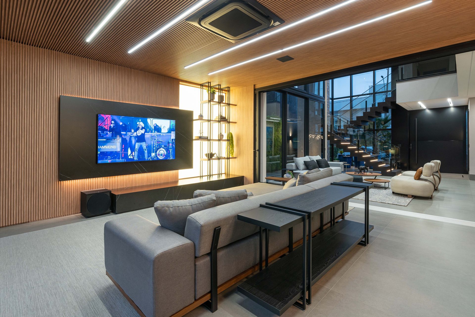 Sala de estar moderna com uma TV grande, sofá cinza e teto de madeira.