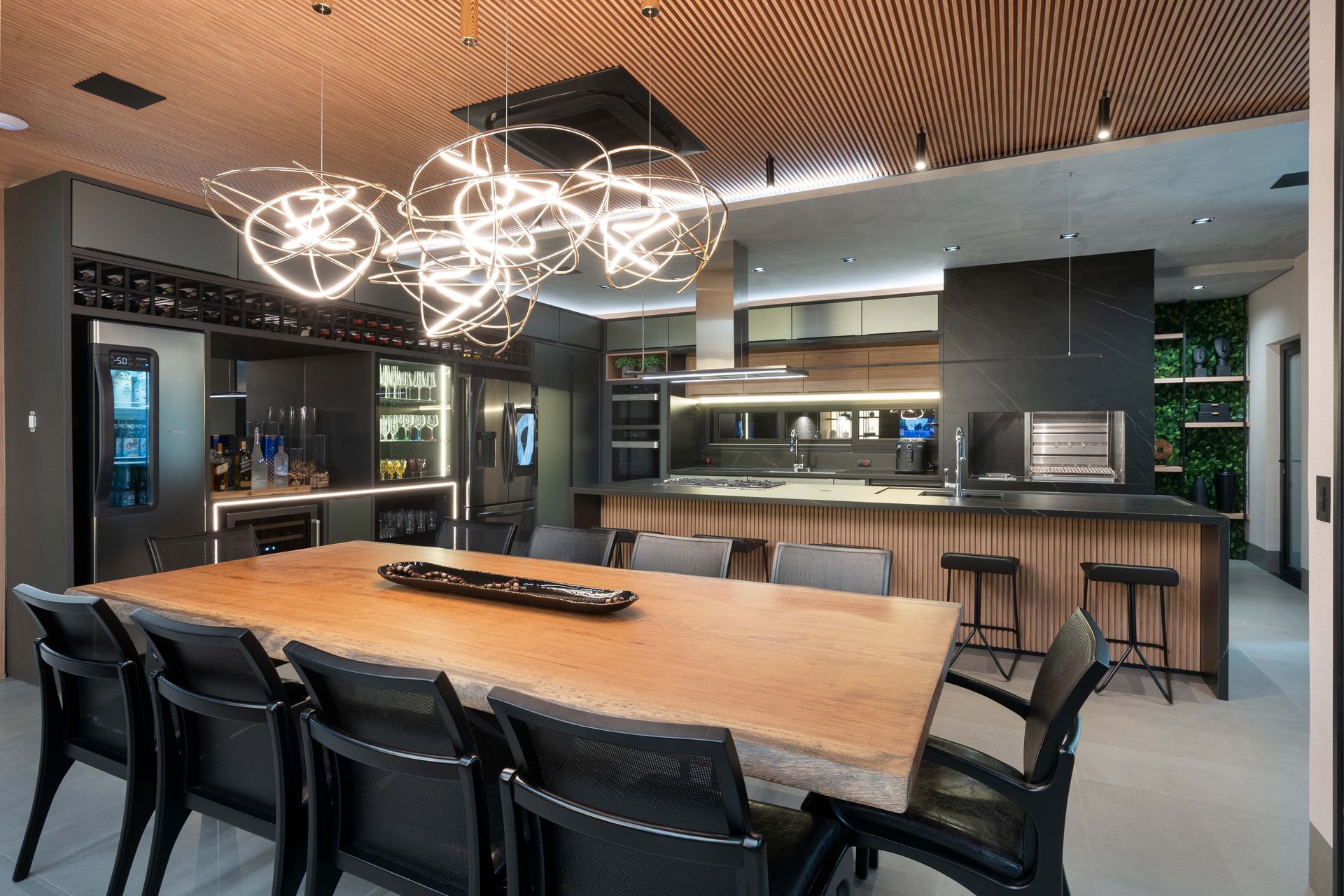 Sala de jantar moderna com grande mesa de madeira, cadeiras pretas e iluminação marcante acima.