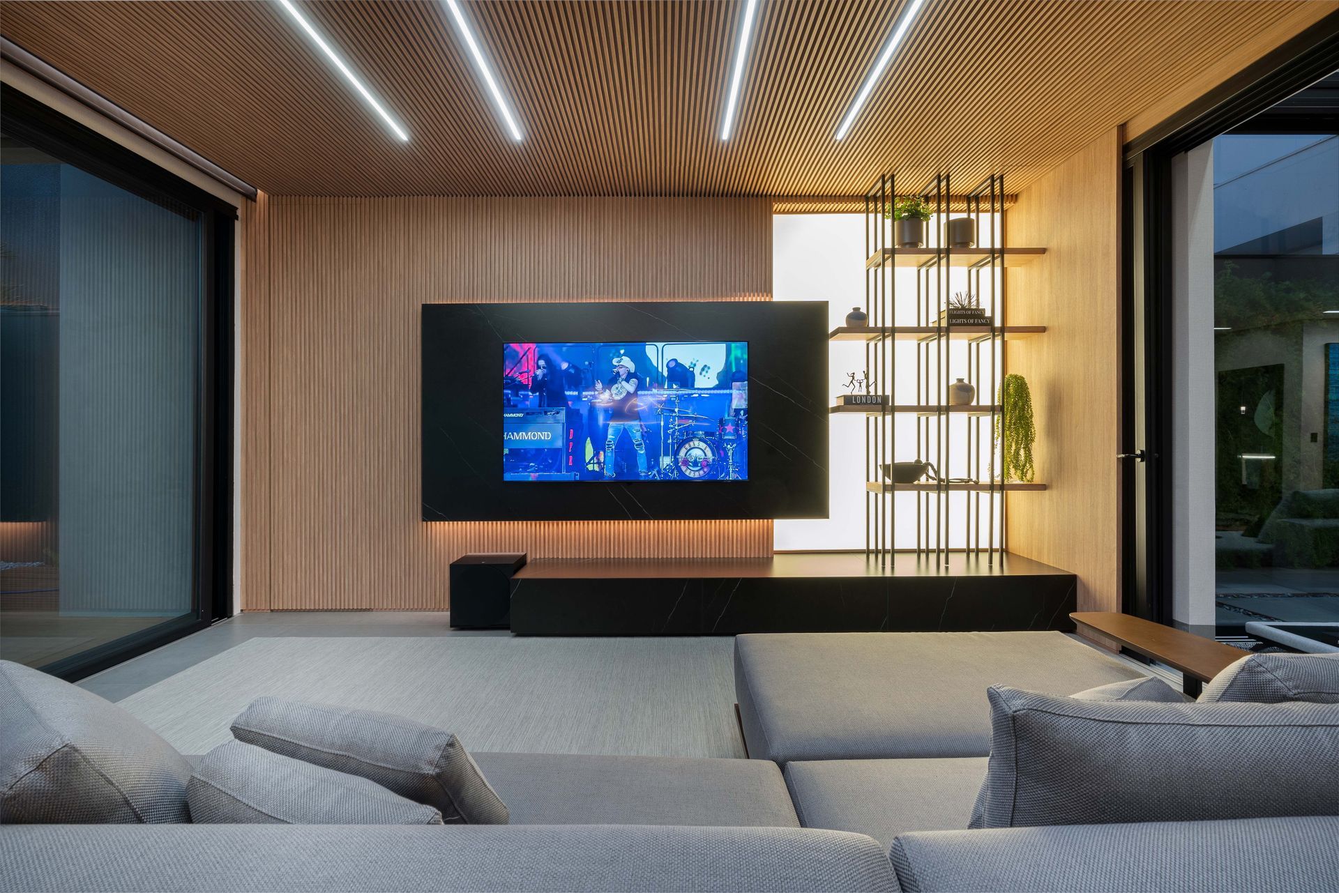 Sala de estar moderna com uma TV grande, sofá secional e detalhes em madeira.