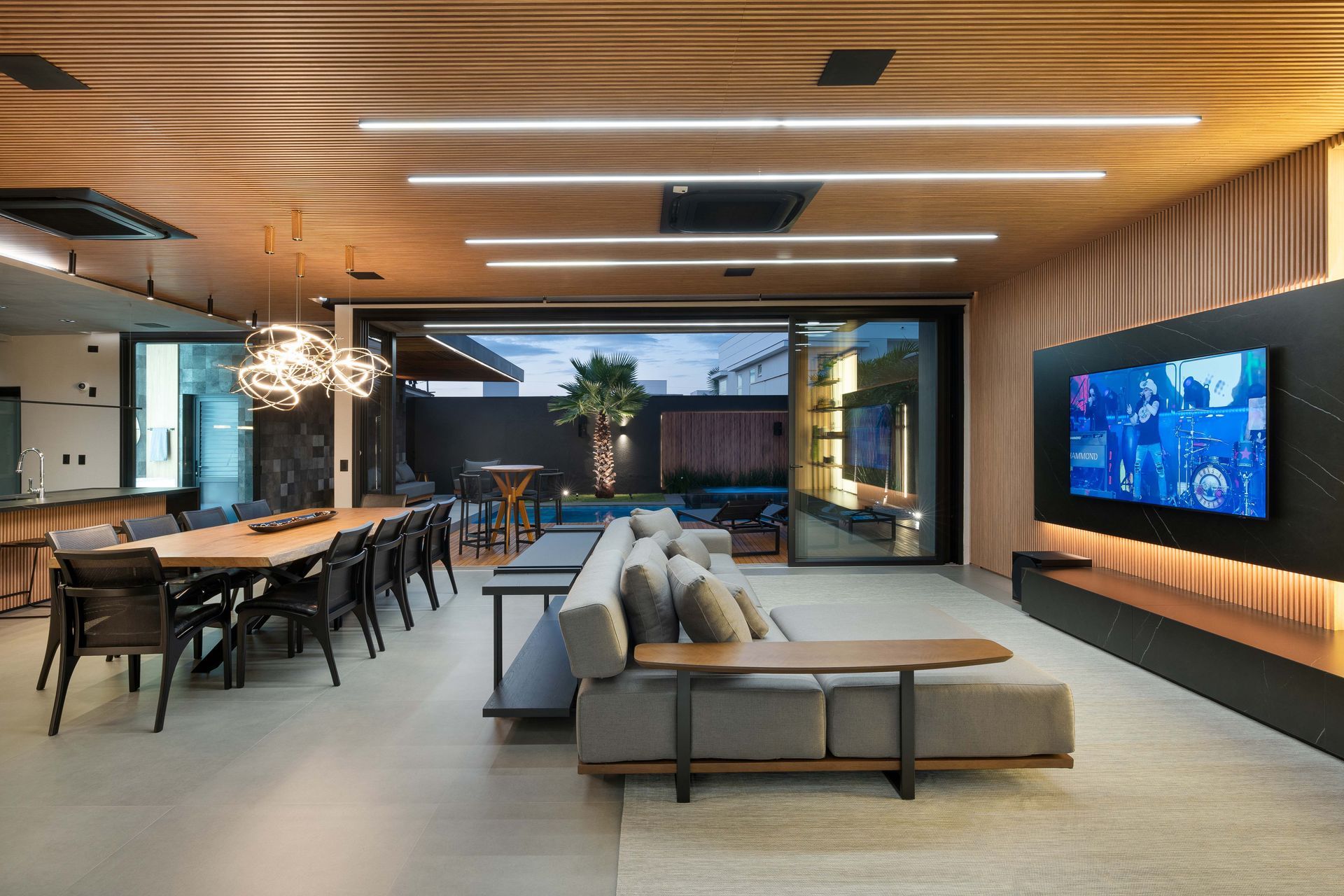 Sala de estar moderna com uma longa mesa de madeira, sofá cinza e vista para o quintal e a piscina.