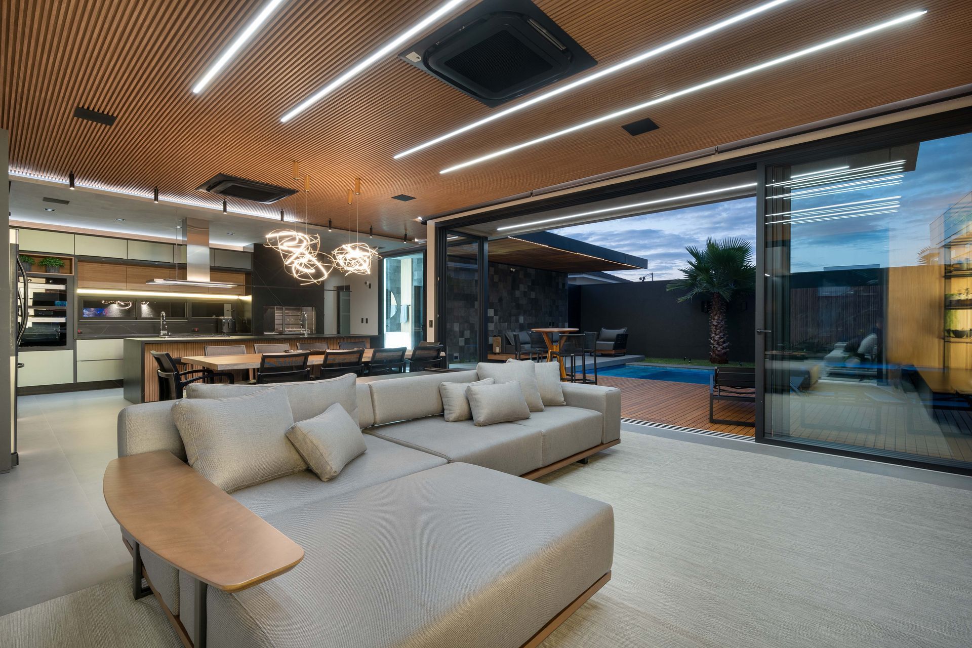 Sala de estar moderna com sofá secional bege, aberta para uma área de piscina através de portas de vidro deslizantes.