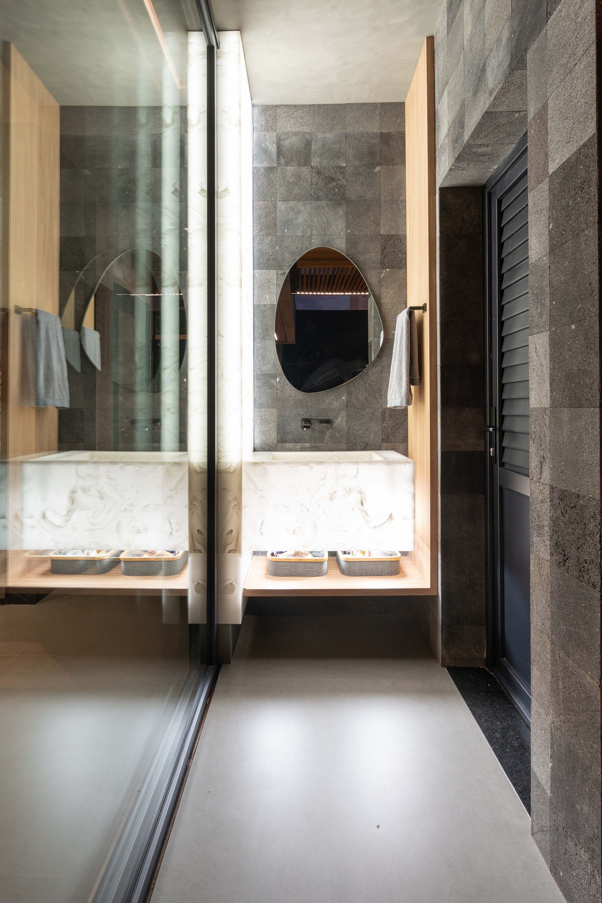 Banheiro moderno com paredes de pedra, piso de concreto e chuveiro de vidro.