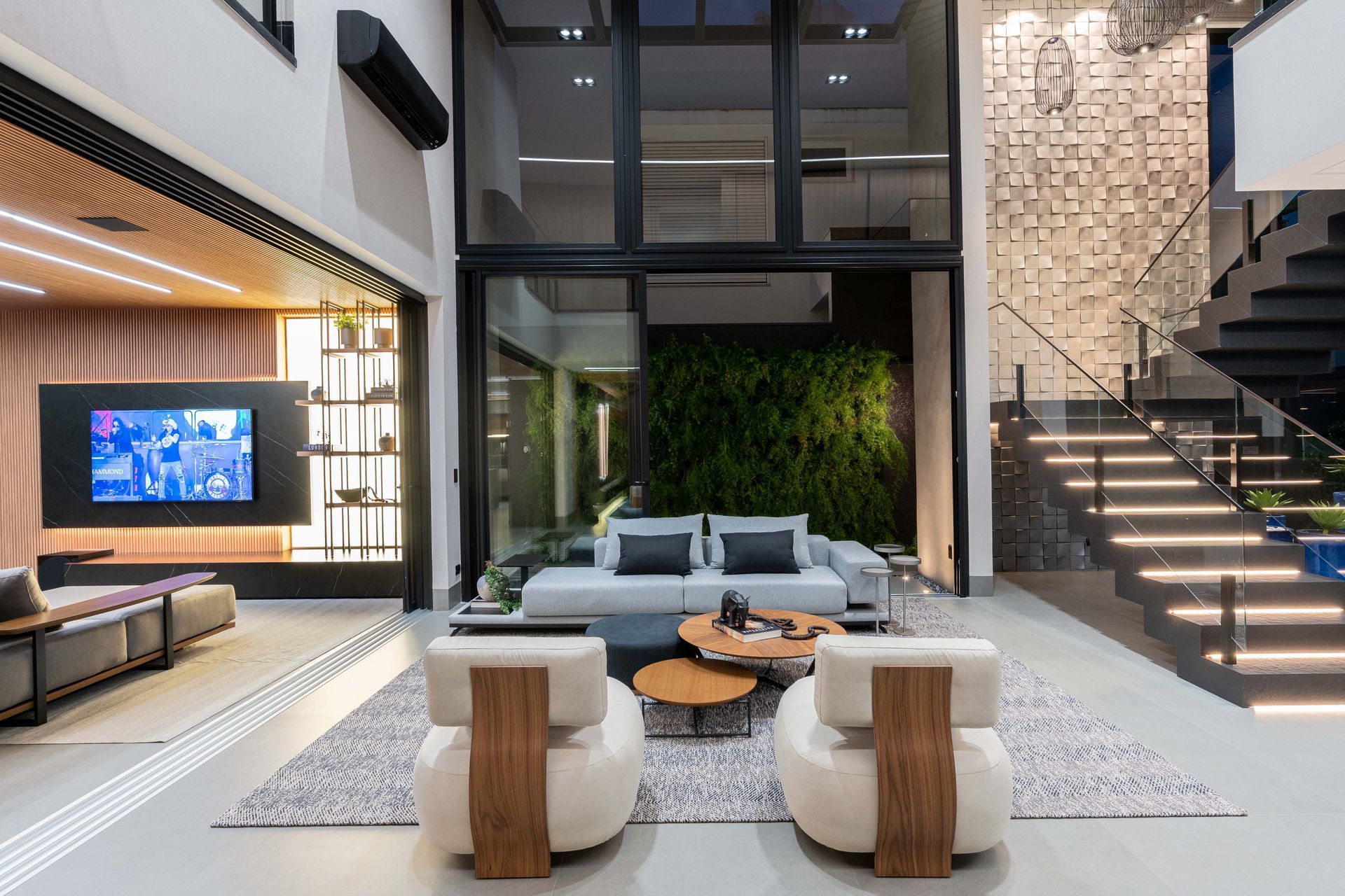 Sala de estar moderna e luxuosa com portas sanfonadas que se abrem para uma parede verde, escada e móveis elegantes.