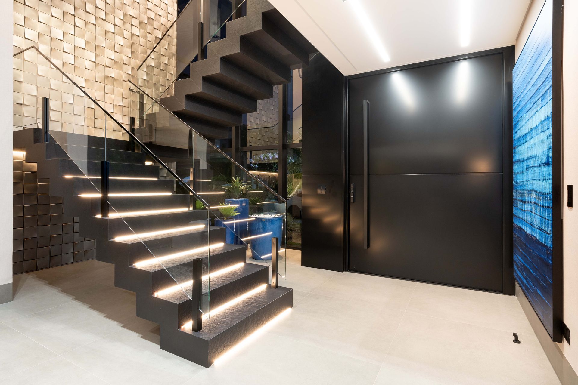 Interior moderno com escadas flutuantes iluminadas por LEDs, porta preta e parede texturizada.
