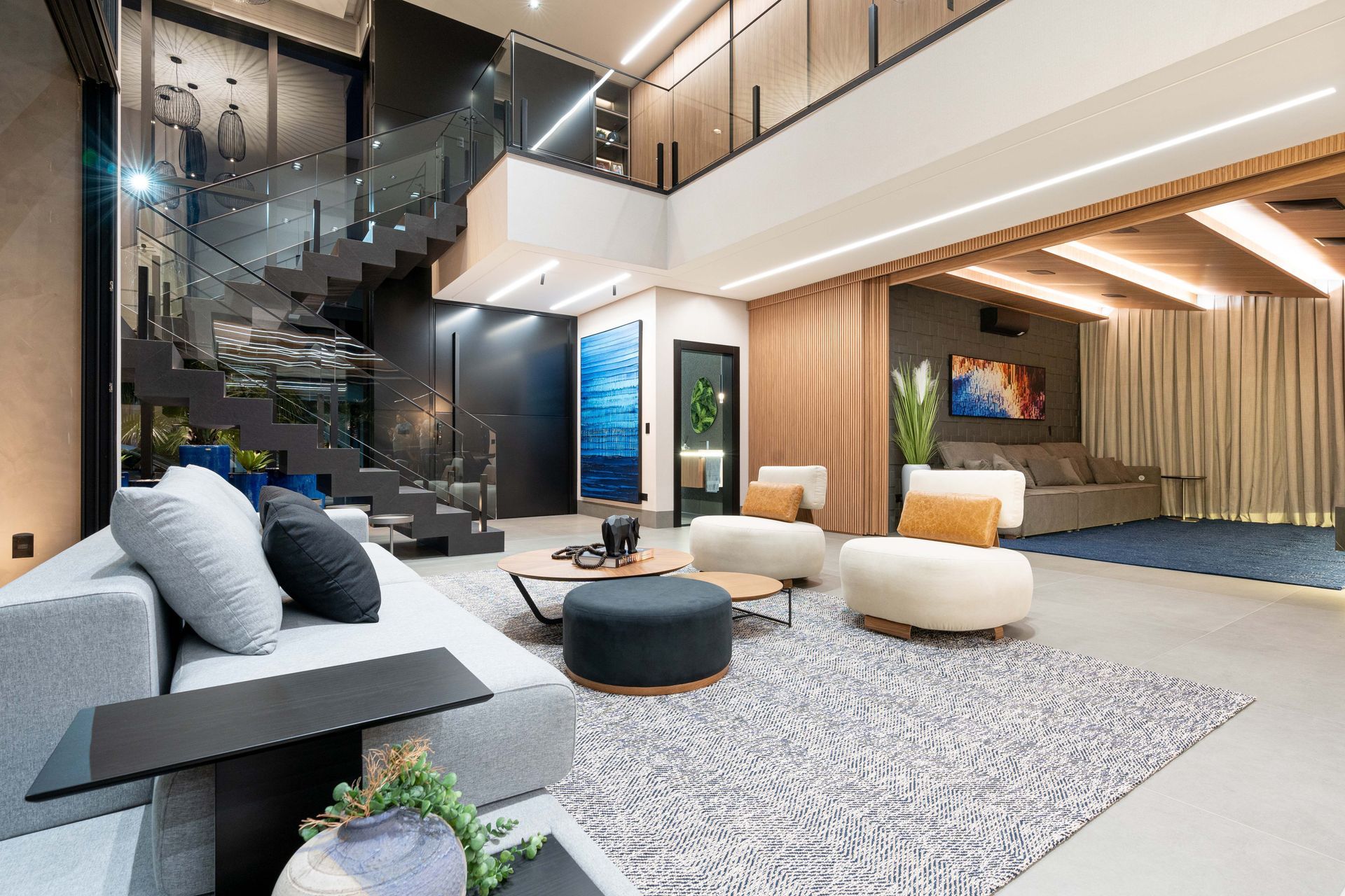 Sala de estar moderna com sofá cinza, tapete estampado e uma escada flutuante.