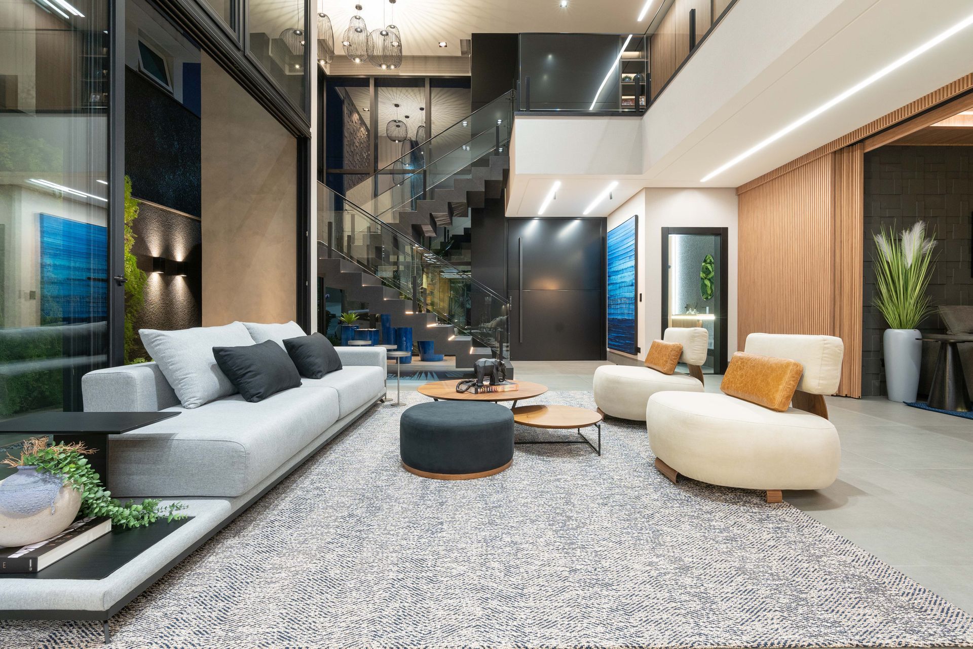 Sala de estar moderna com sofá cinza, cadeiras curvas e uma escada.