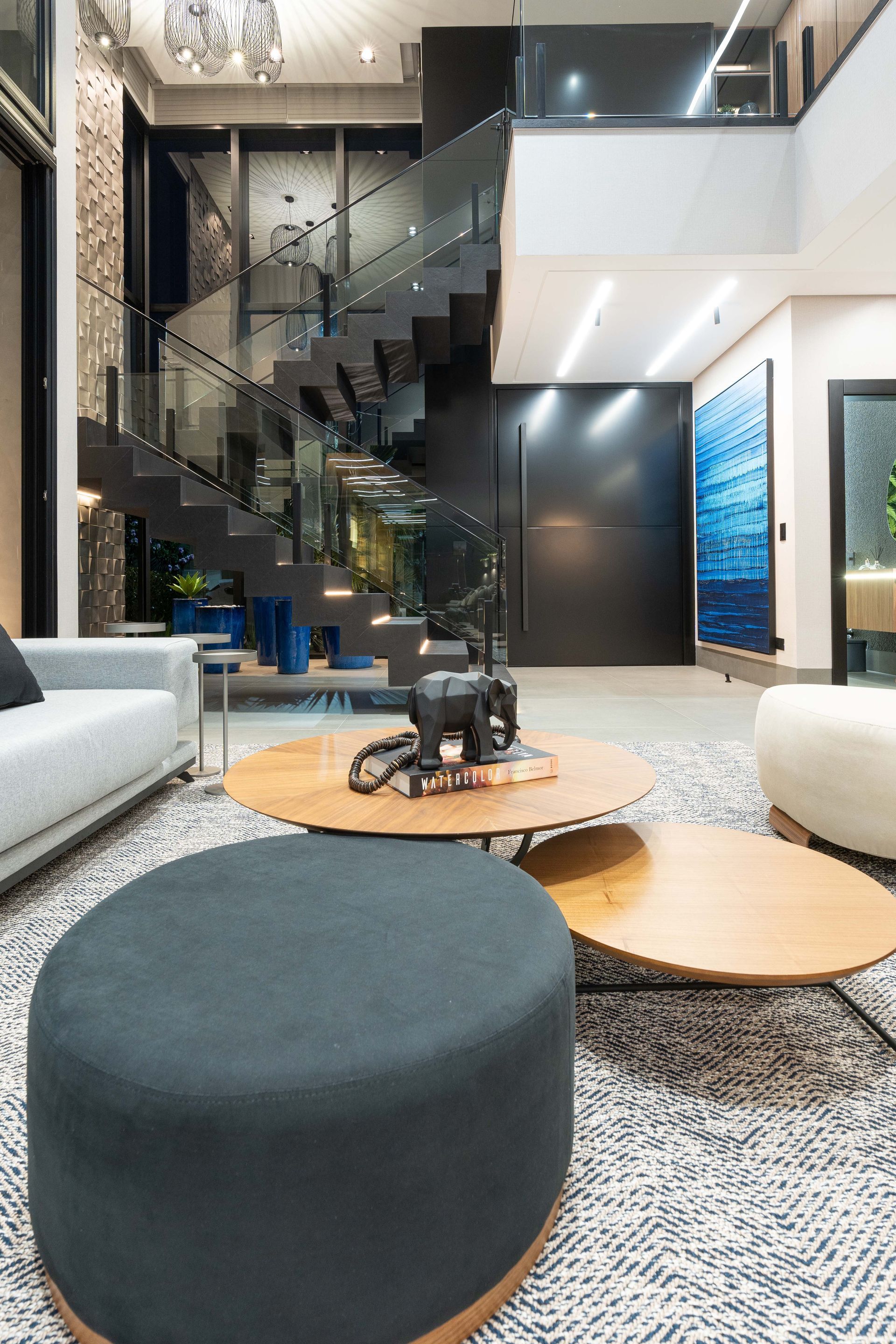 Sala de estar moderna com escada em espiral, mesas de centro e tapete estampado.