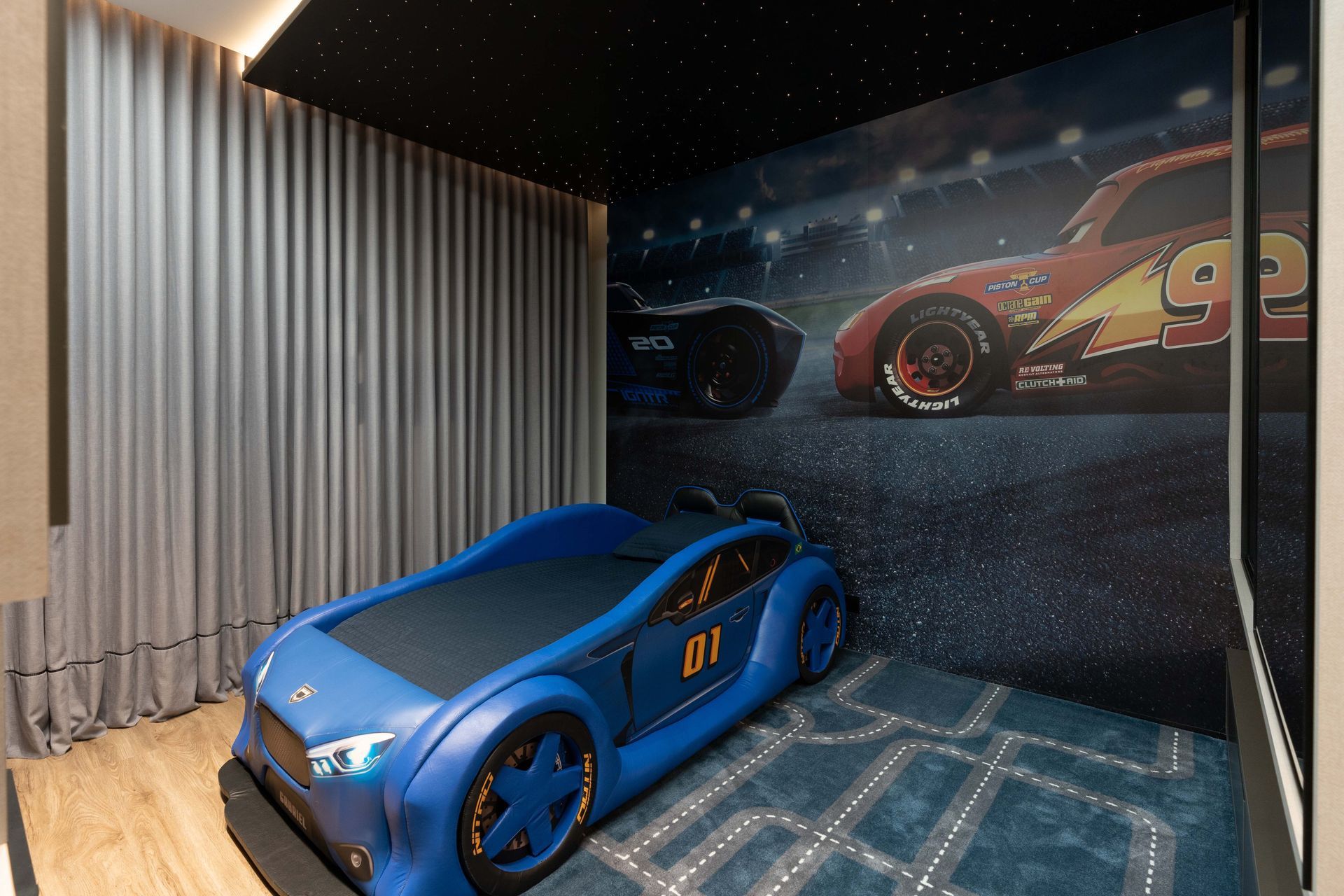 Um quarto com tema de carros, com uma cama azul de carro de corrida e um mural do filme Carros ao fundo.