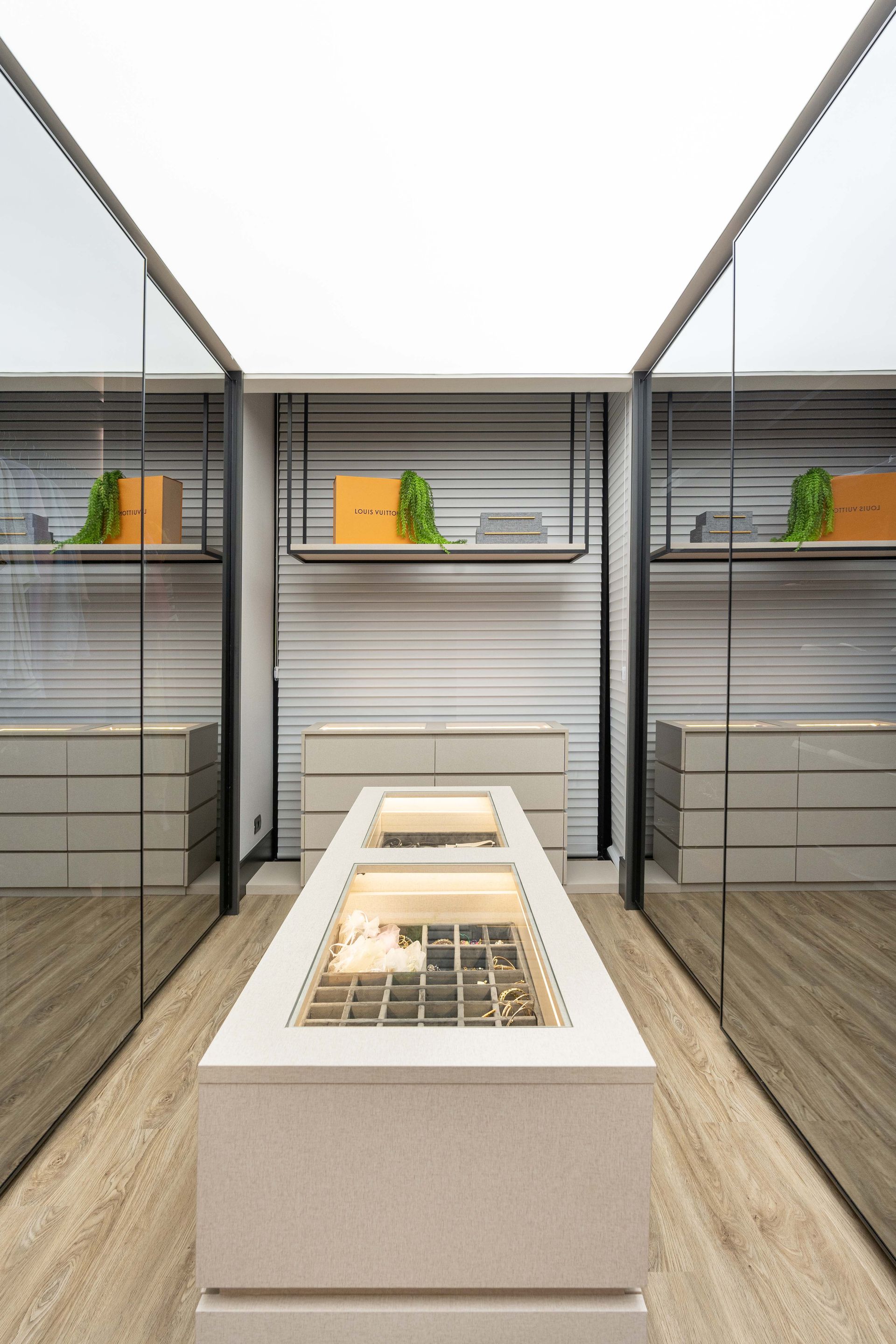 Interior de joalheria: ilha de exposição, espelhos refletivos, prateleiras com decoração.