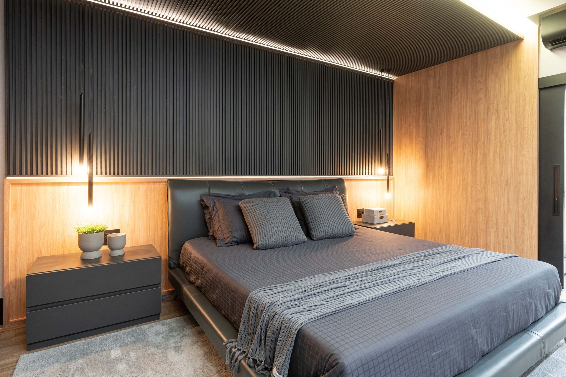 Quarto moderno com cama e parede cinza escuro, realçado por painéis de madeira e iluminação suave.