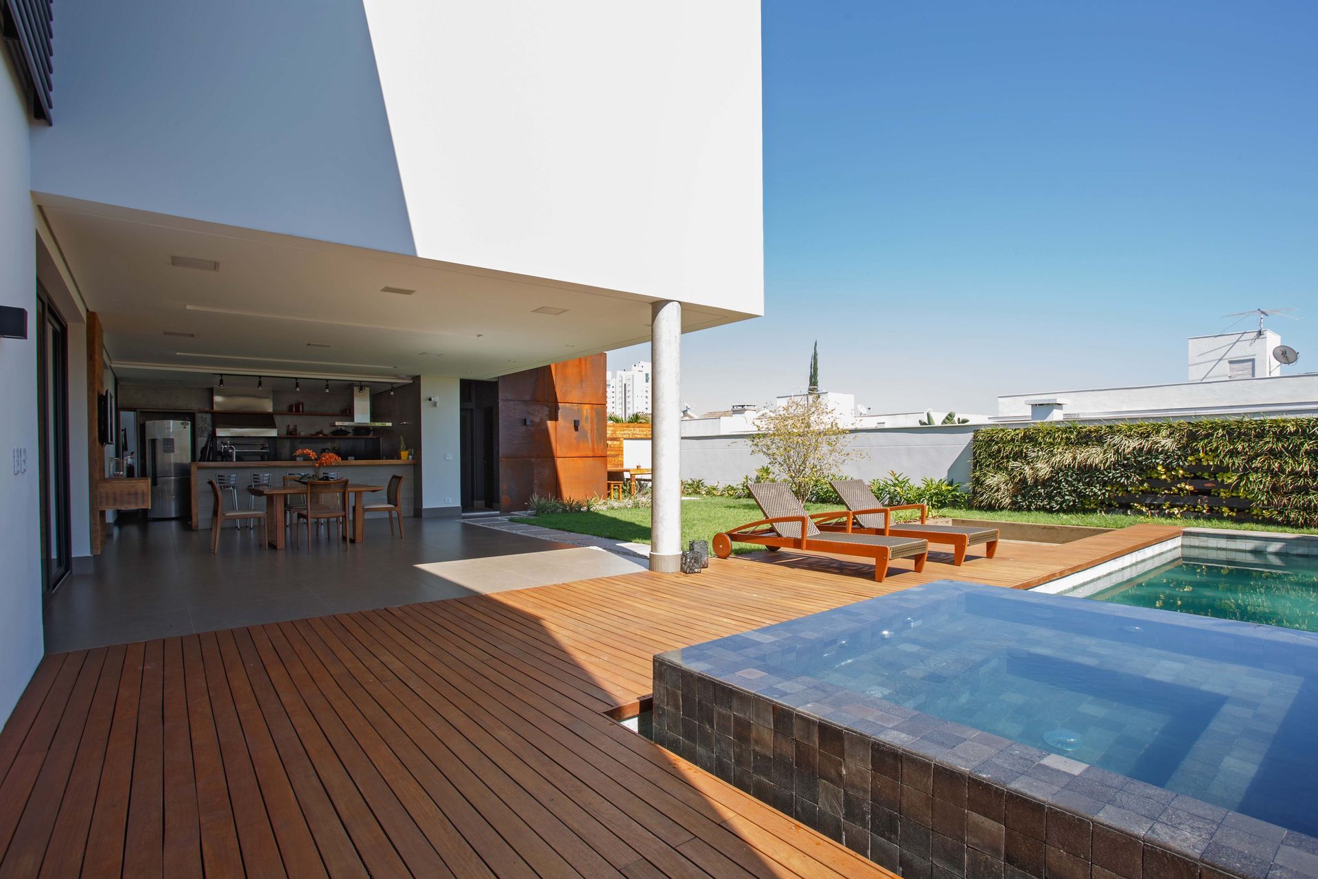 Exterior de uma casa moderna com deck, piscina e espreguiçadeiras em um dia ensolarado.