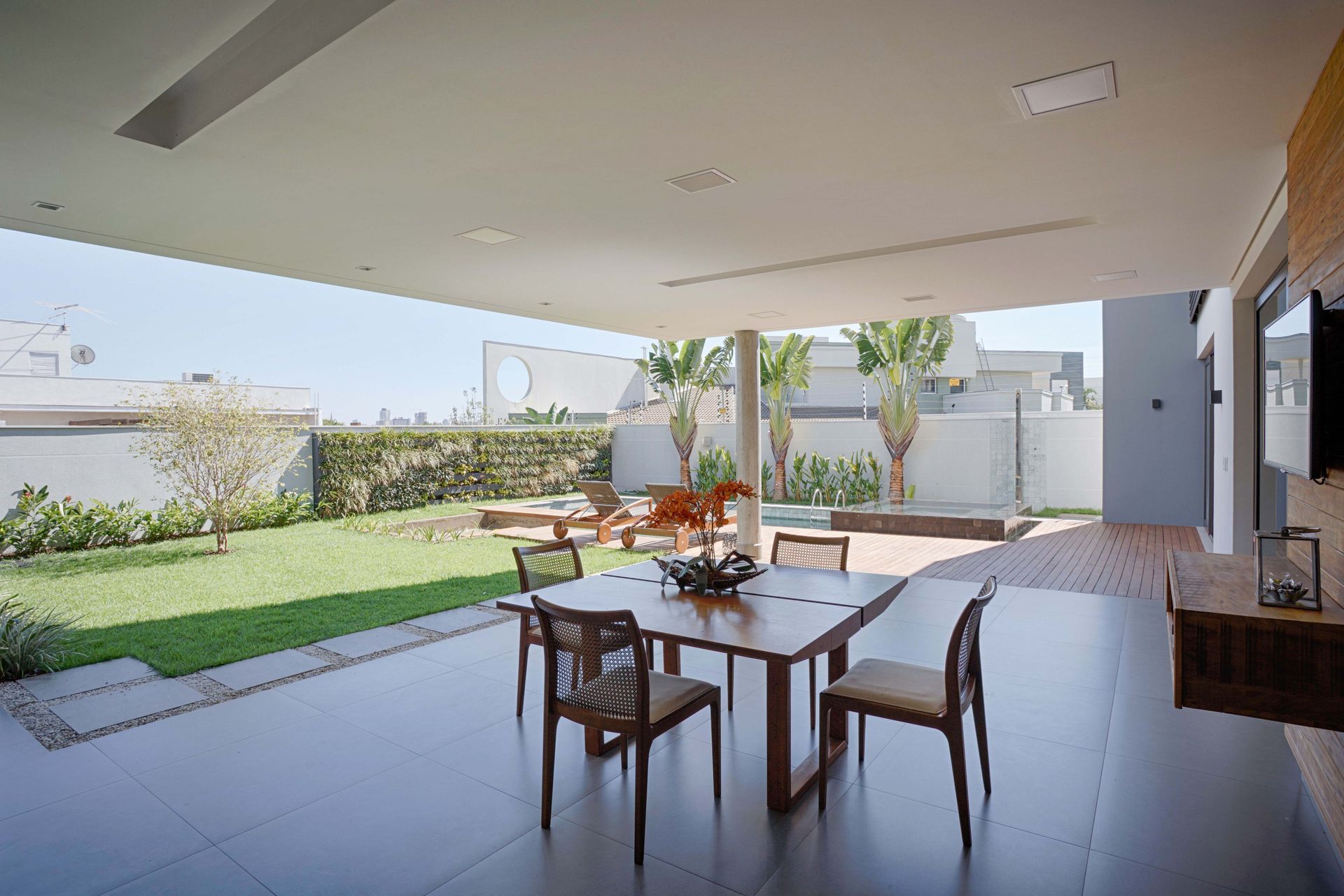 Área de jantar ao ar livre com mesa de madeira, cadeiras e um gramado verde.