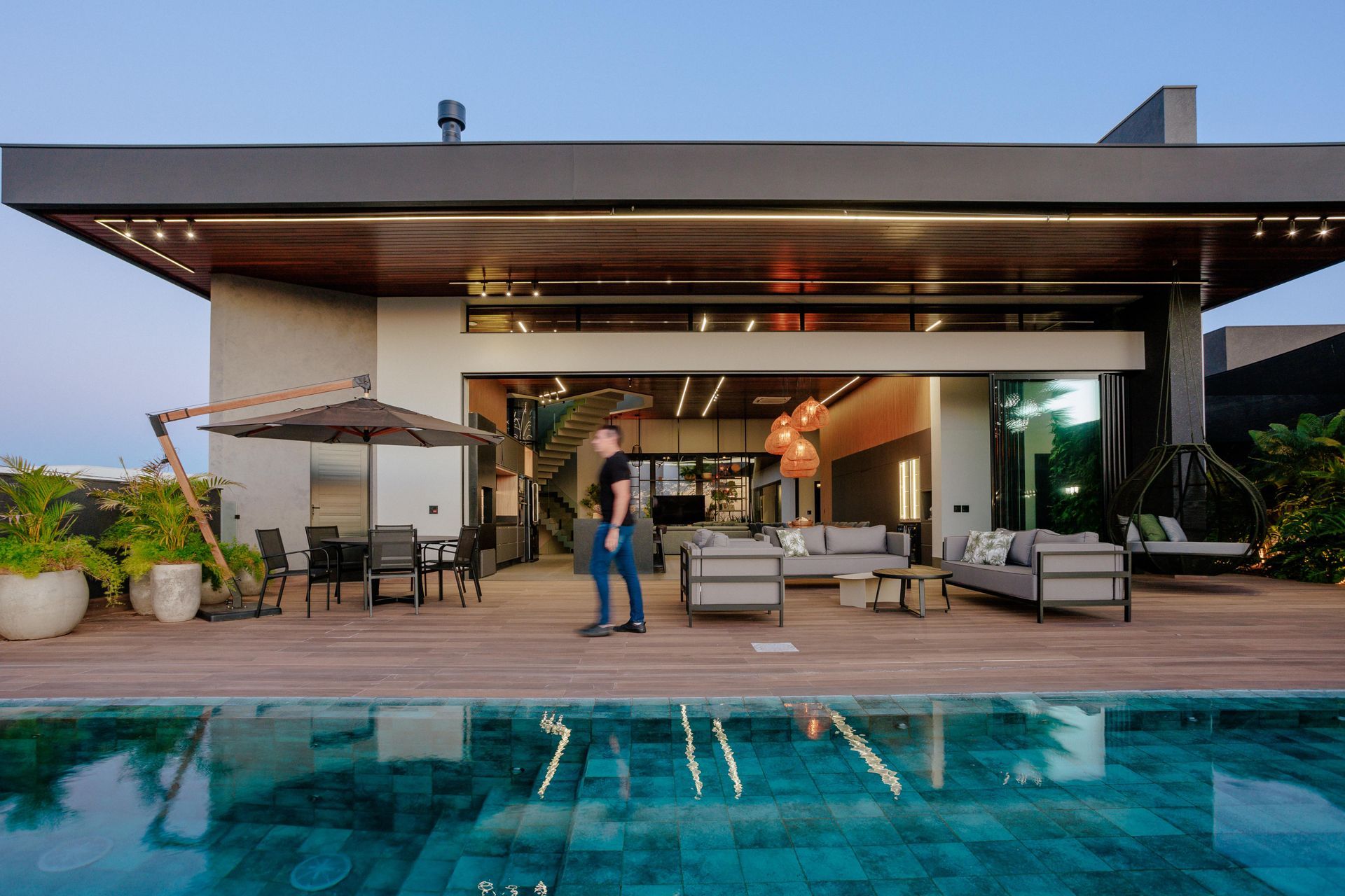 Casa moderna com portas abertas para uma piscina, com assentos ao ar livre e uma pessoa em pé no pátio.