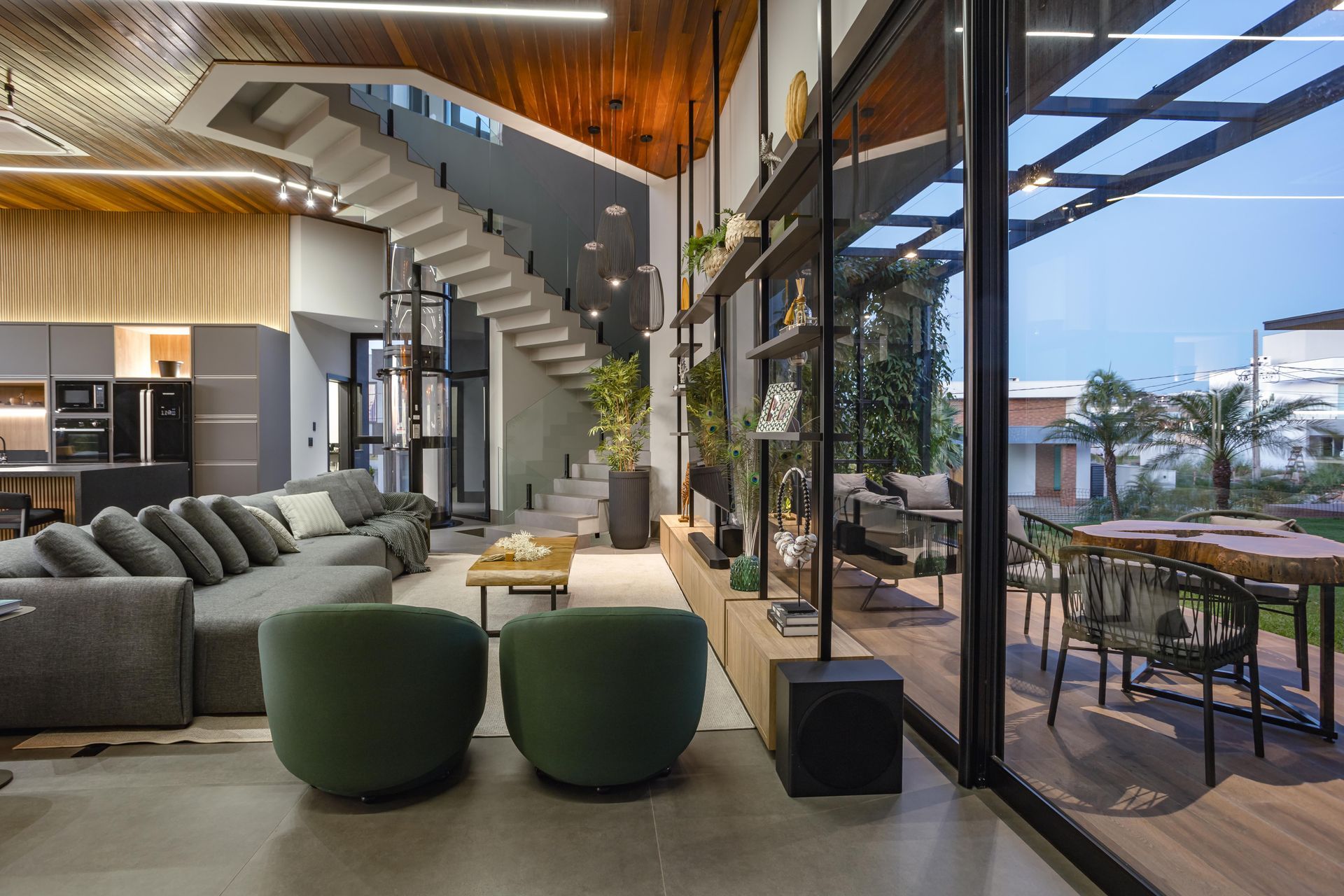 Sala de estar moderna com janelas grandes, escadas e área de jantar ao ar livre.