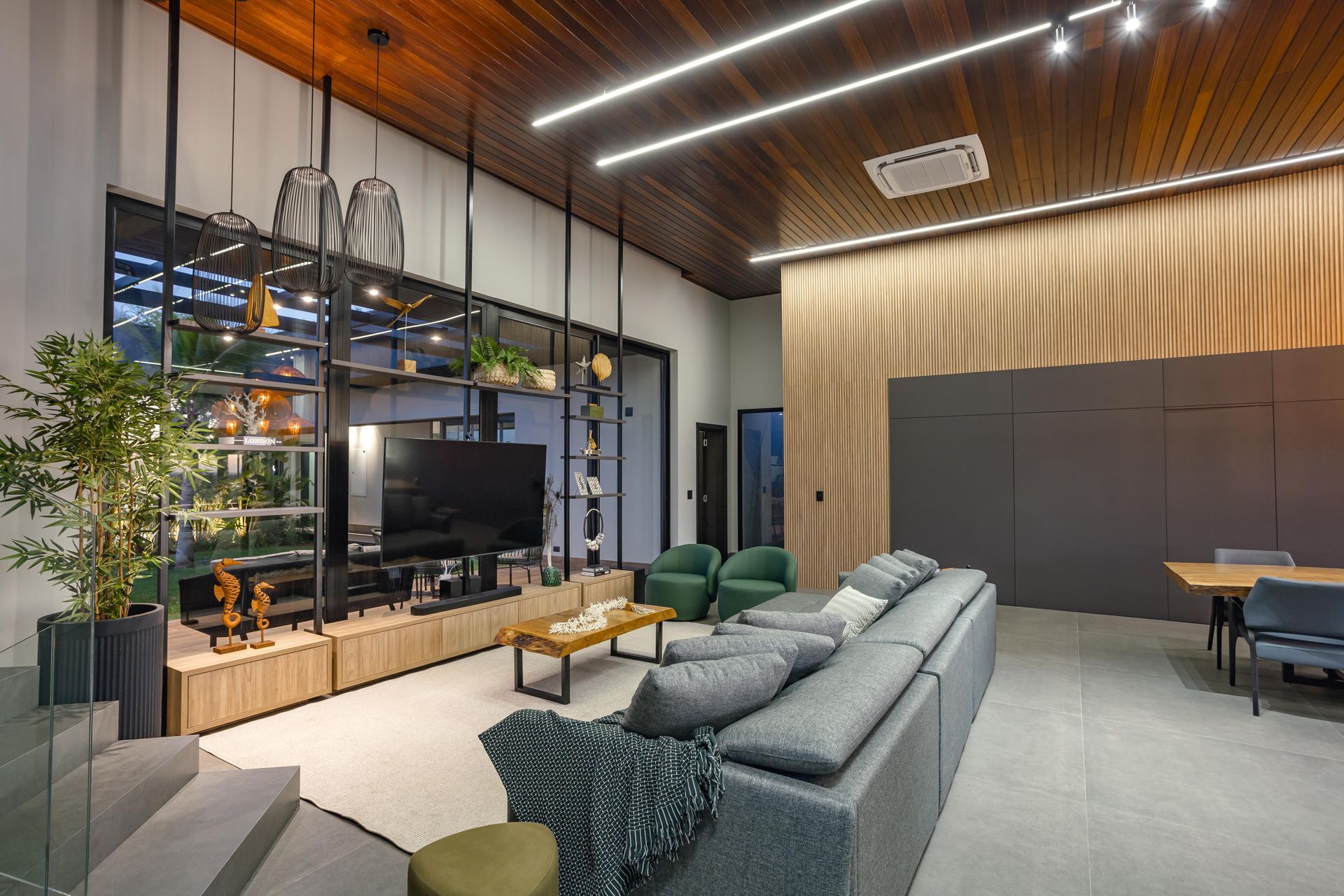 Sala de estar moderna com teto de madeira, paredes cinzas, sofá, TV, estantes e escadas.