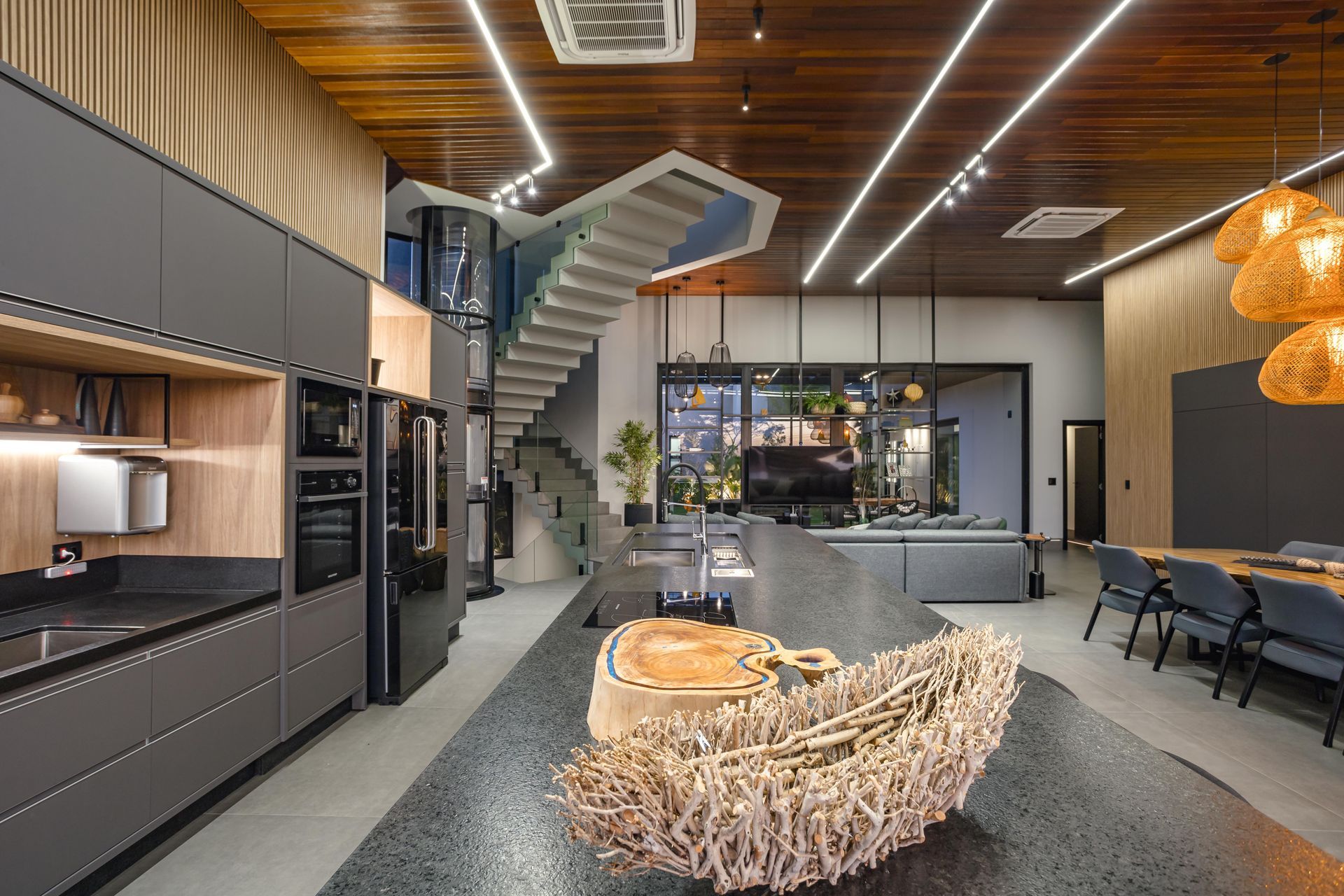 Cozinha moderna com armários cinza escuro, ilha e escada que leva ao andar de cima.