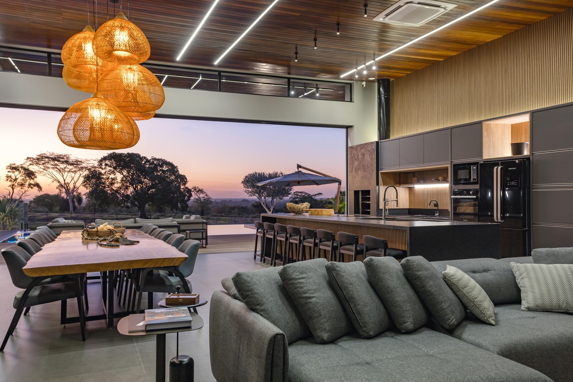 Sala de estar em conceito aberto com uma grande porta aberta, mesa de jantar, cozinha e um sofá secional cinza.