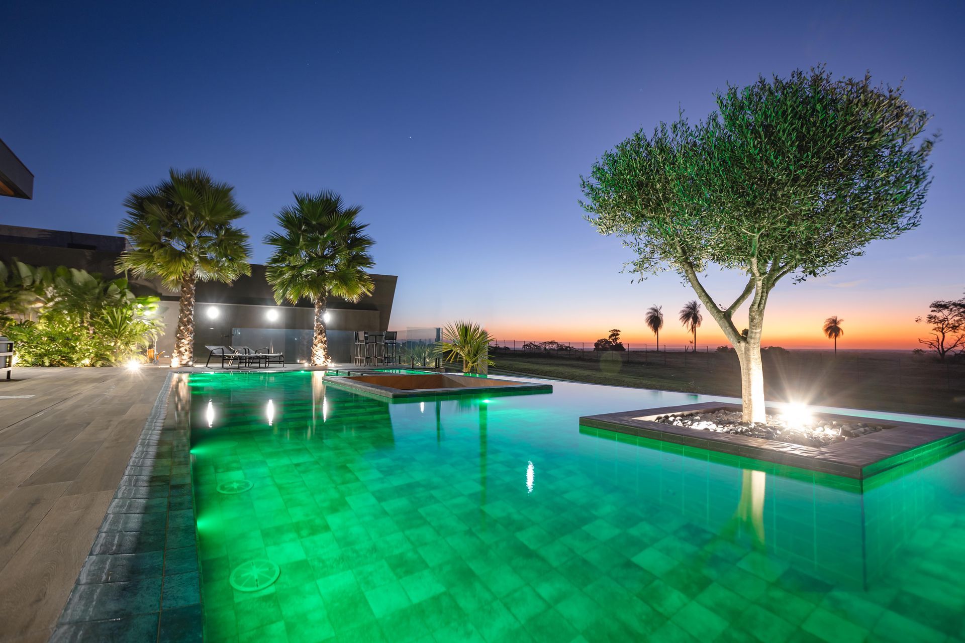 Piscina ao entardecer com uma árvore e água verde. Céu limpo com cores do pôr do sol desaparecendo.